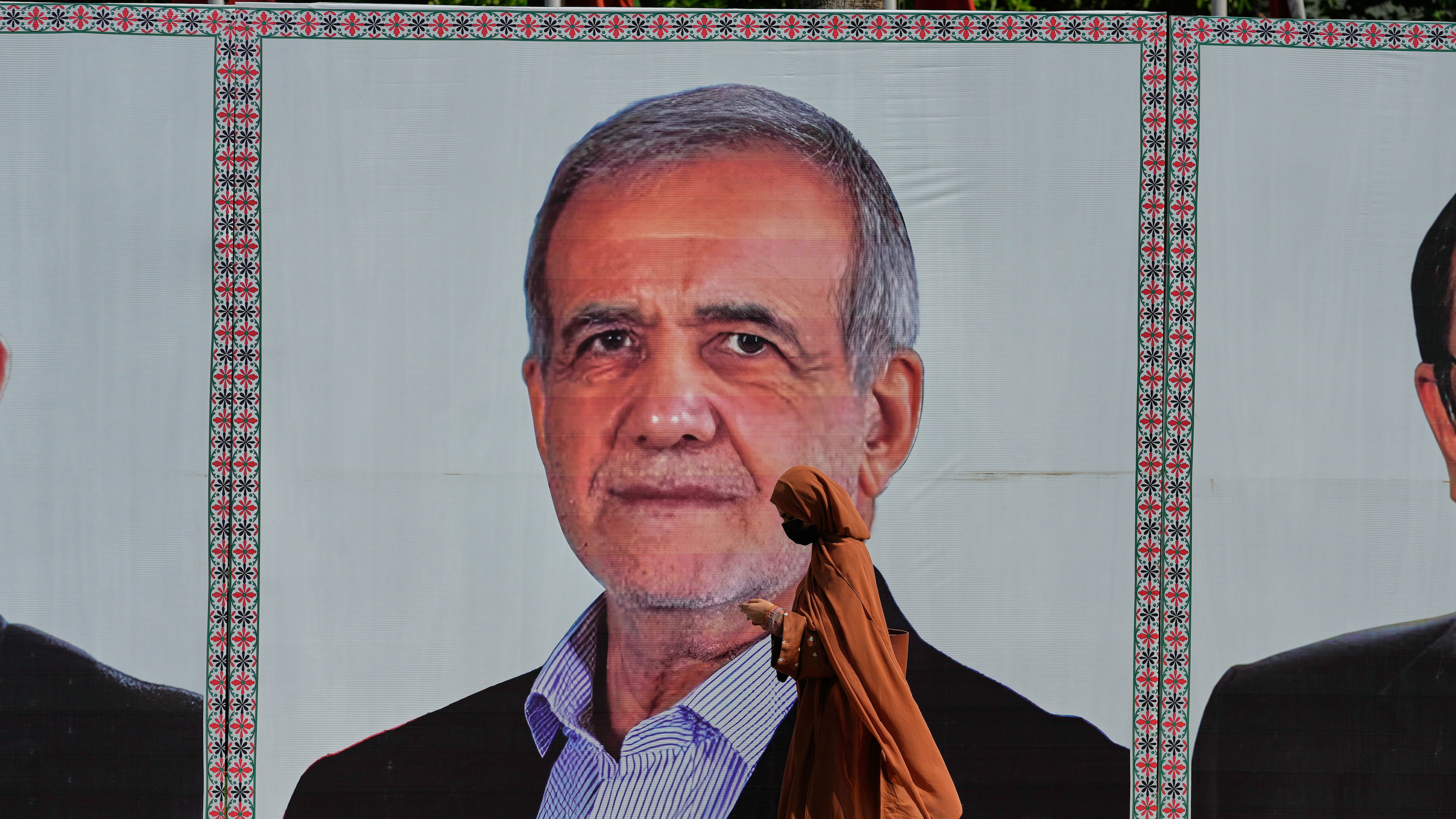 A woman walks past a welcoming billboard featuring Iranian President Masoud Pezeshkian along a roadside in Islamabad, Pakistan, Tuesday, June 23, 2026. (AP Photo/Anjum Naveed)