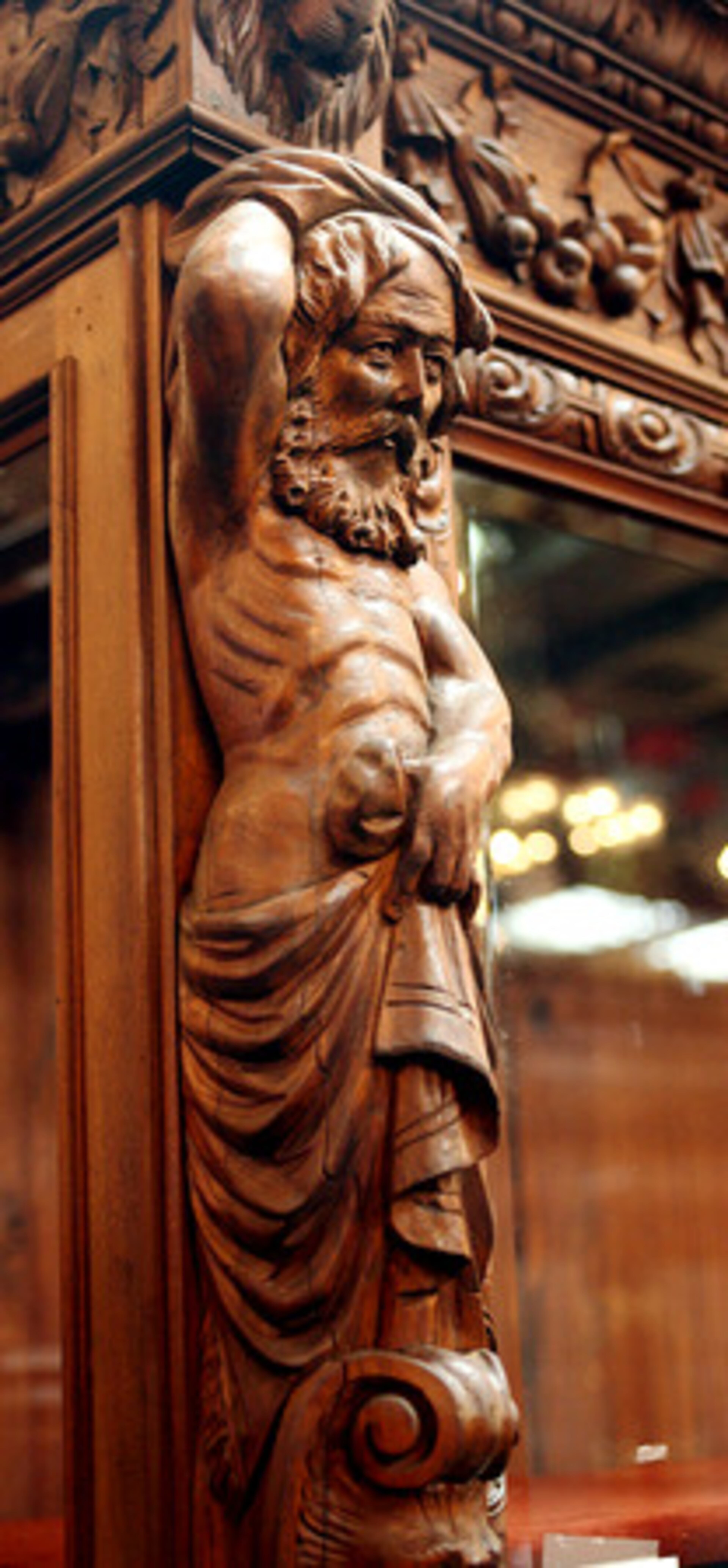 A detail from the vitrine, which features intricately carved details including an atlas mask, eagles, lion heads, male figures and fruits.