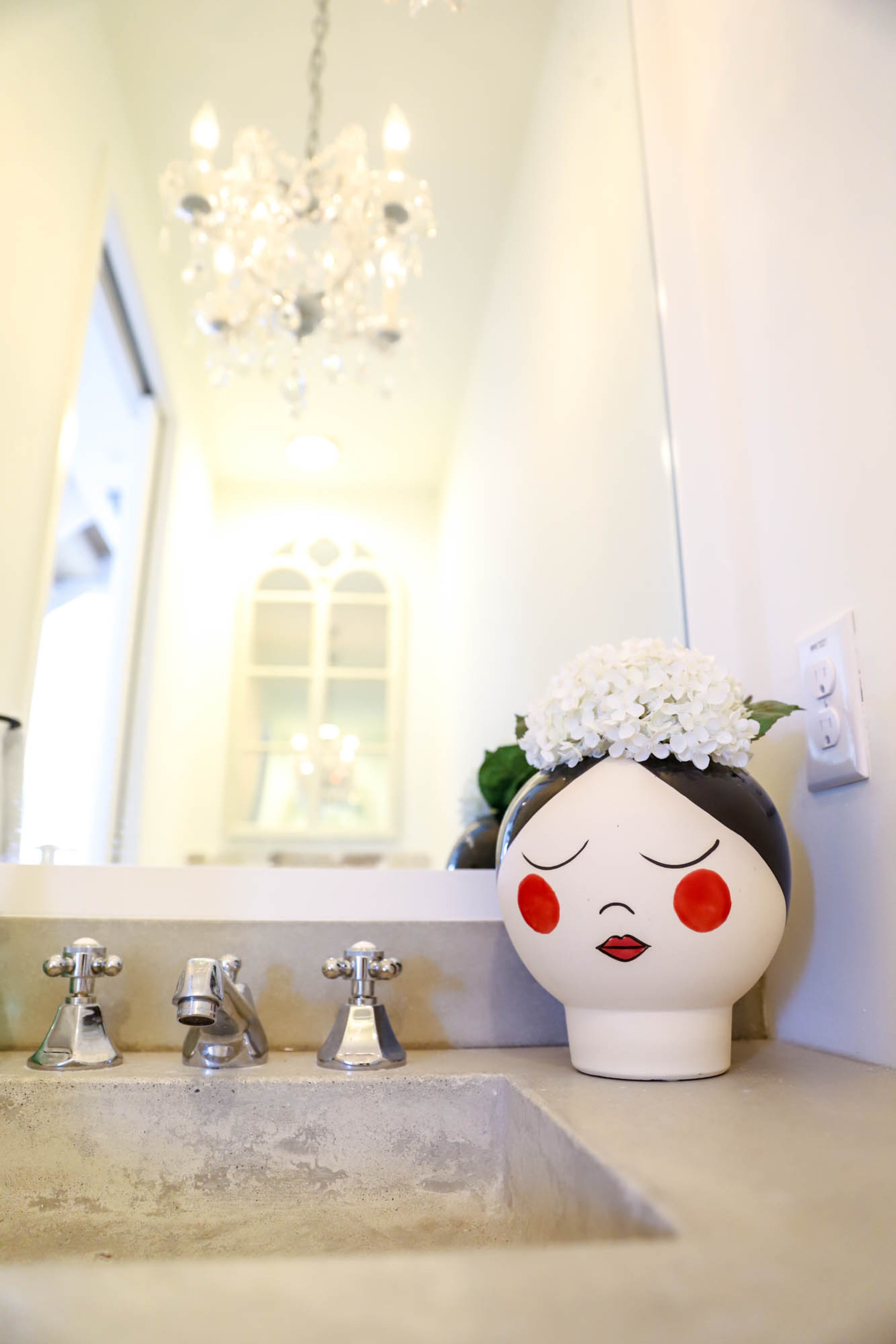 A whimsical planter from Tuesday Morning sits on the concrete counter in the powder room. The bathroom features a full-length mirror above the sink and a cathedral window mirror on the other end.