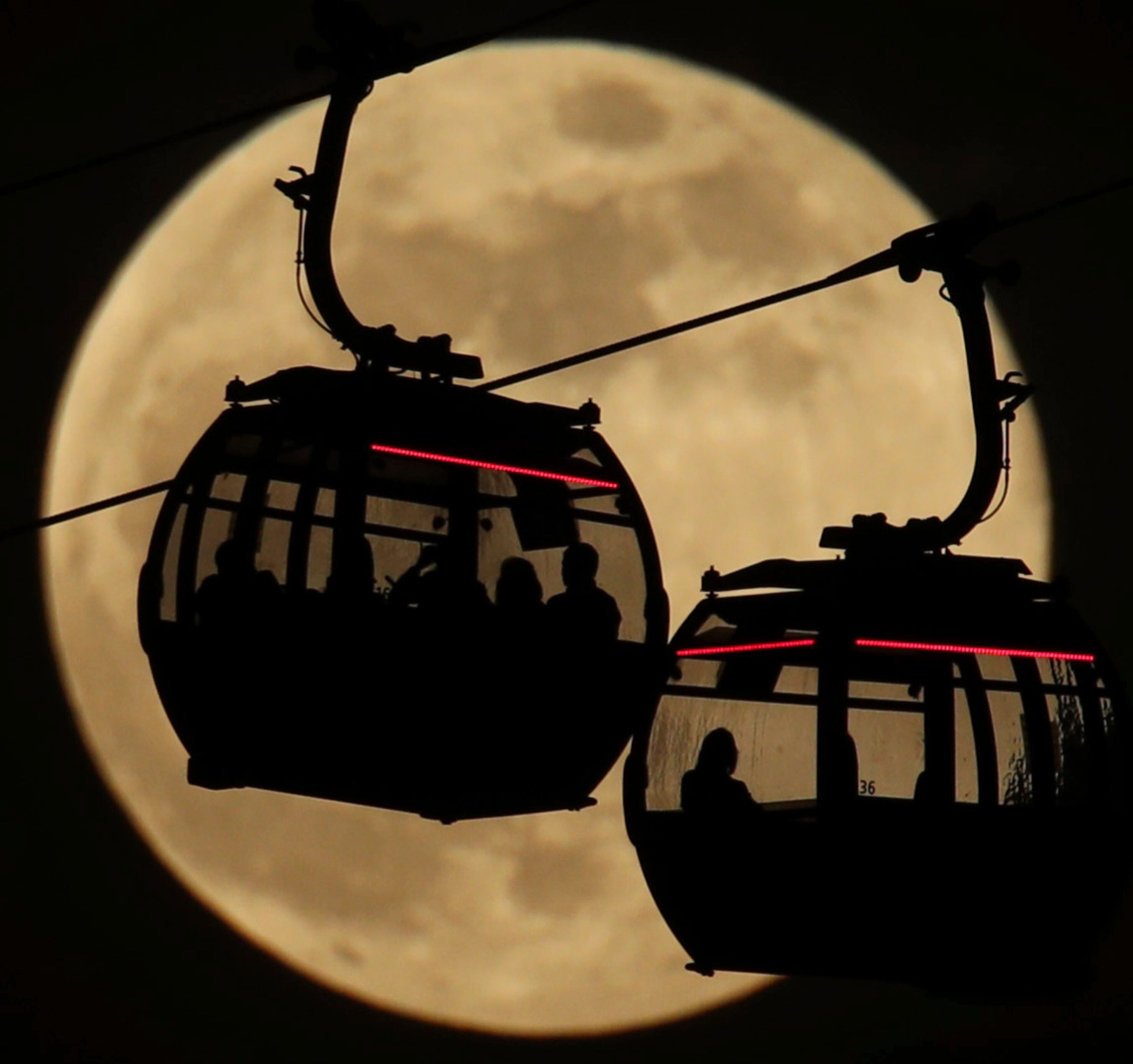 Emirates Air Line cable cars are silhouetted against the backdrop of the 'supermoon' in Greenwich, London, Tuesday, Feb. 19, 2019. Tuesday's full moon, or supermoon, appears brighter and bigger than other full moons because it is close to its perigee, which is the closest point in its orbit to Earth. (Yui Mok/PA via AP)