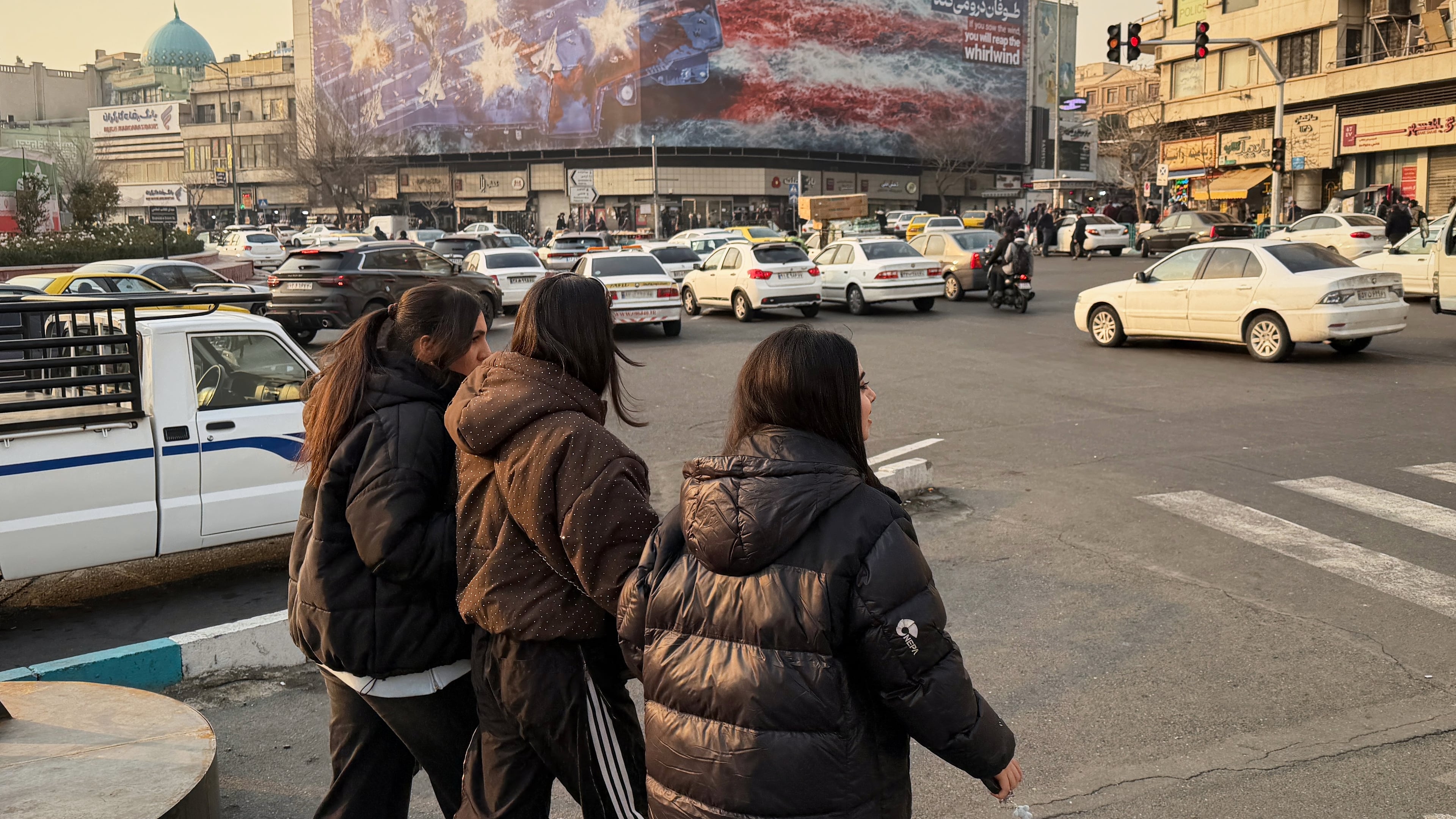 People walk in front a billboard with graphic showing a U.S aircraft carrier with damaged fighter jets on its deck, and sign reading in Farsi and English: "If you sow the wind, you'll reap whirlwind," at the Enqelab-e-Eslami (Islamic Revolution) square, in Tehran, Iran, Sunday, Jan. 25, 2026. (AP Photo/Vahid Salemi)