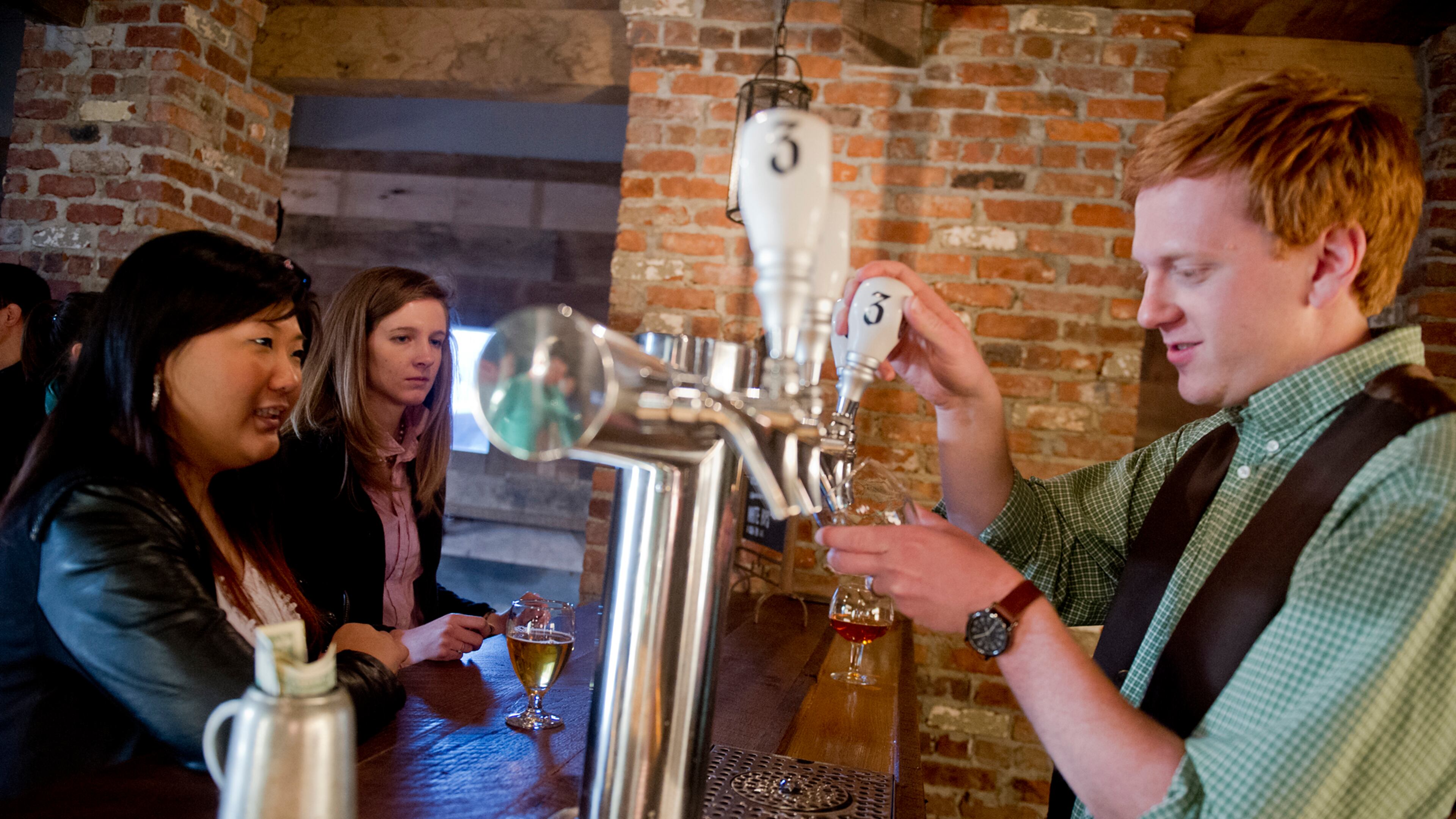 Danny Ritchie (right) pours a beer for Hannah Cho (left) and Natalie Rogol at Three Taverns Craft Brewery in Decatur in this file photo.