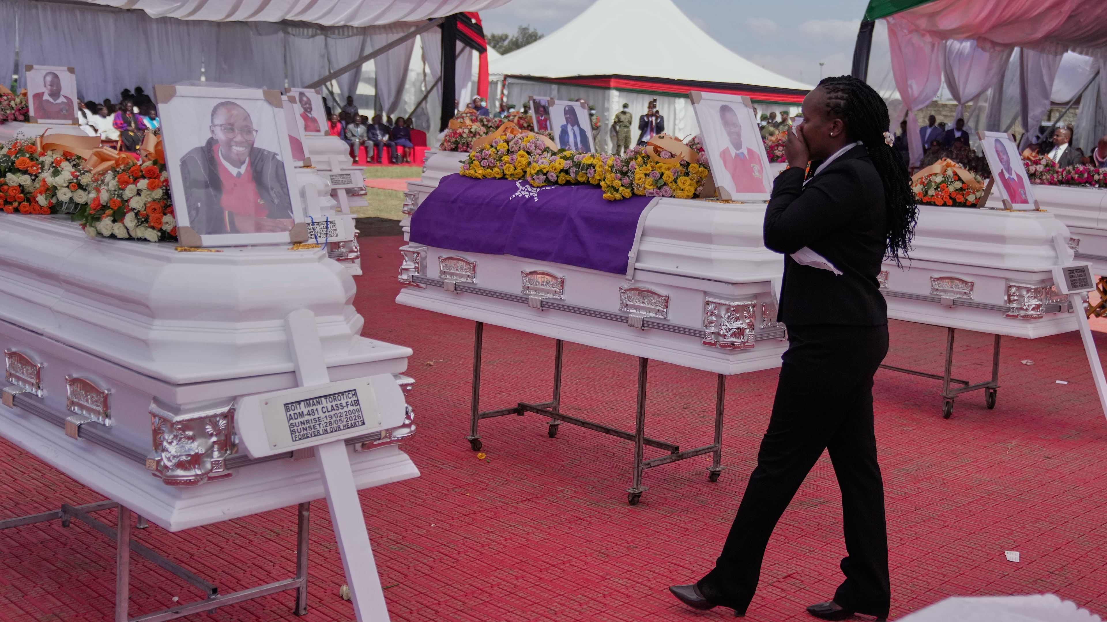A mourner reacts as she stands between caskets carrying the remains of the 16 girls who died in the Utumishi Academy school fire during a memorial service at Gilgil Stadium, Nakuru County, Kenya, Friday, June 12, 2026. (AP Photo/Brian Inganga)