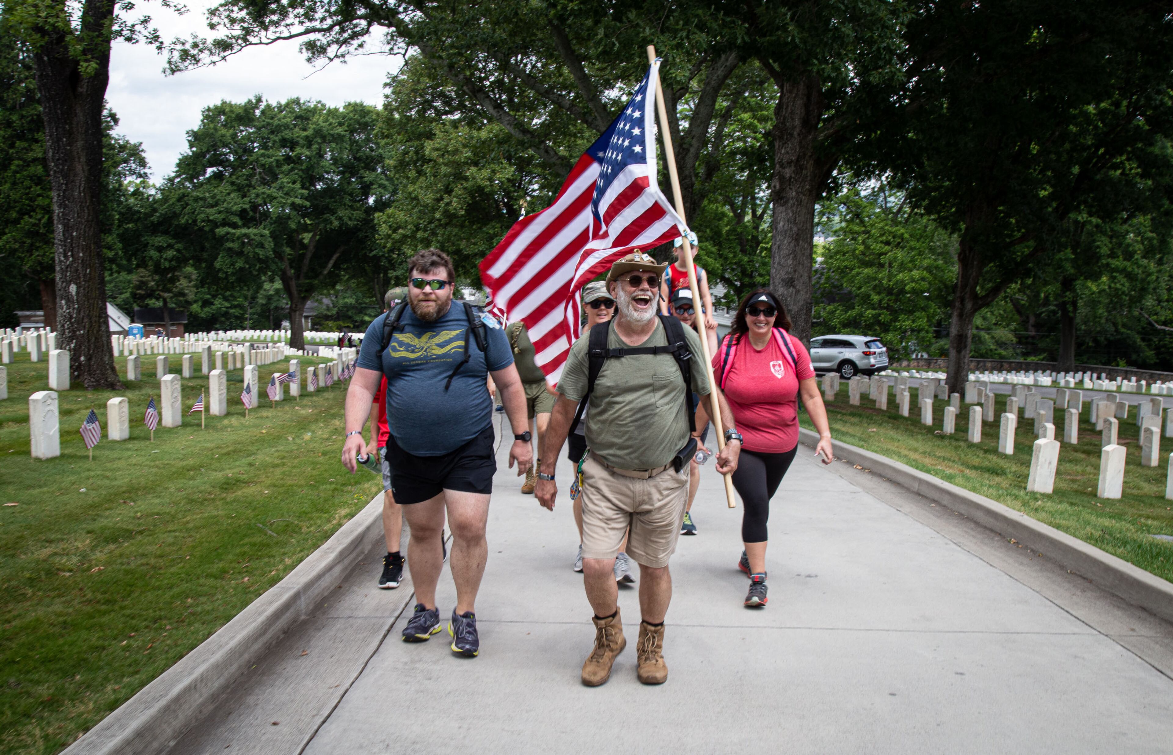 John Tackett leads a group of people into the Marietta National Cemetery while carrying a flag that has flown over the USS Arizona memorial at Pearl Harbor. STEVE SCHAEFER FOR THE ATLANTA JOURNAL-CONSTITUTION