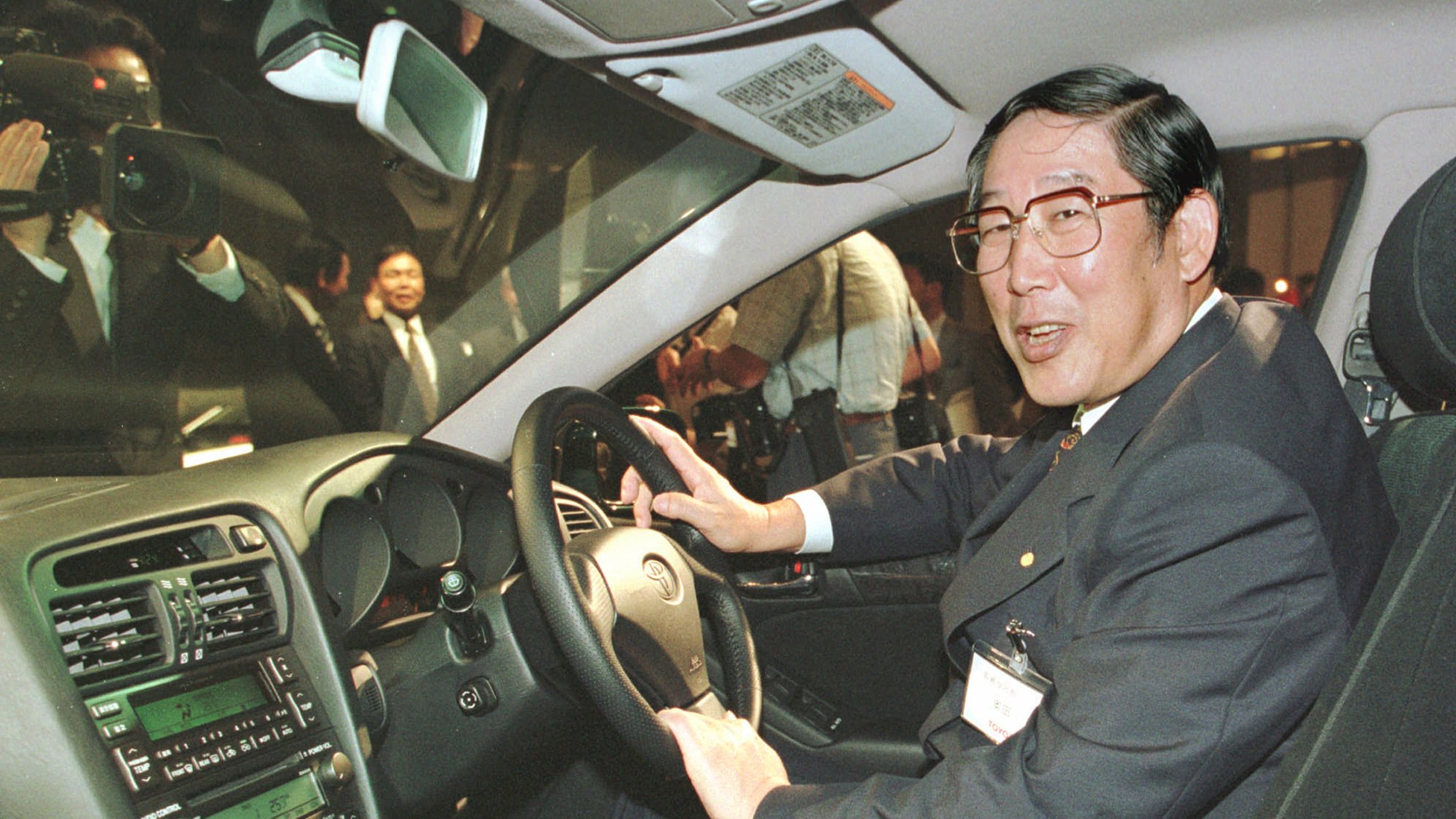 FILE - Hiroshi Okuda, then, president of Toyota Motor Corp., smiles as he sits at the steering wheel of the "Aristo," Toyota's remodeled sports sedan during a press conference at a Tokyo hotel, Aug. 27, 1997. (AP Photo/Shizuo Kambayashi, File)