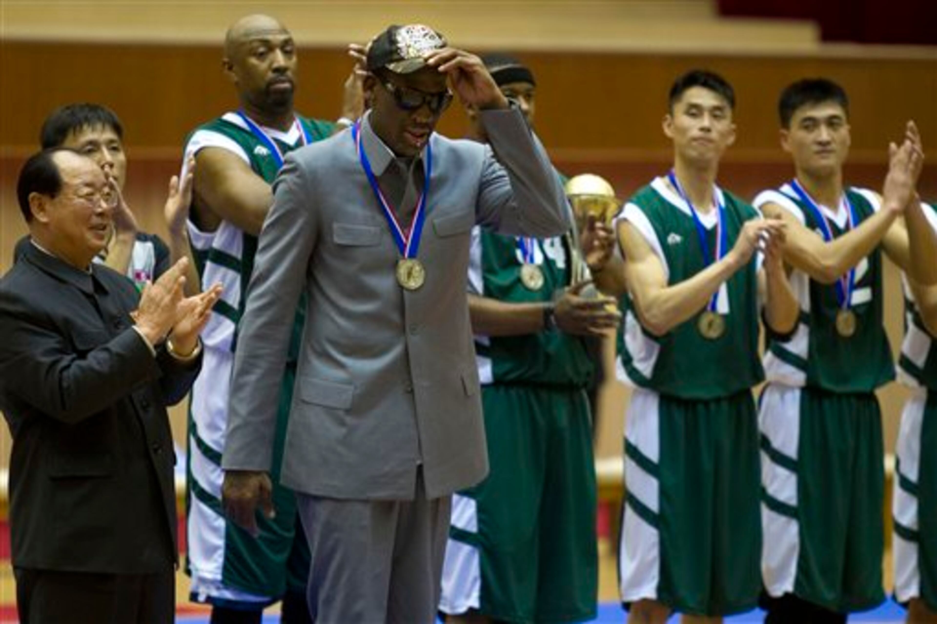 Dennis Rodman tips his hat as U.S. and North Korean basketball players applaud at the end of an exhibition basketball game at an indoor stadium in Pyongyang, North Korea on Wednesday, Jan. 8, 2014. Behind him at right is former NBA player Vin Baker. (AP Photo/Kim Kwang Hyon)