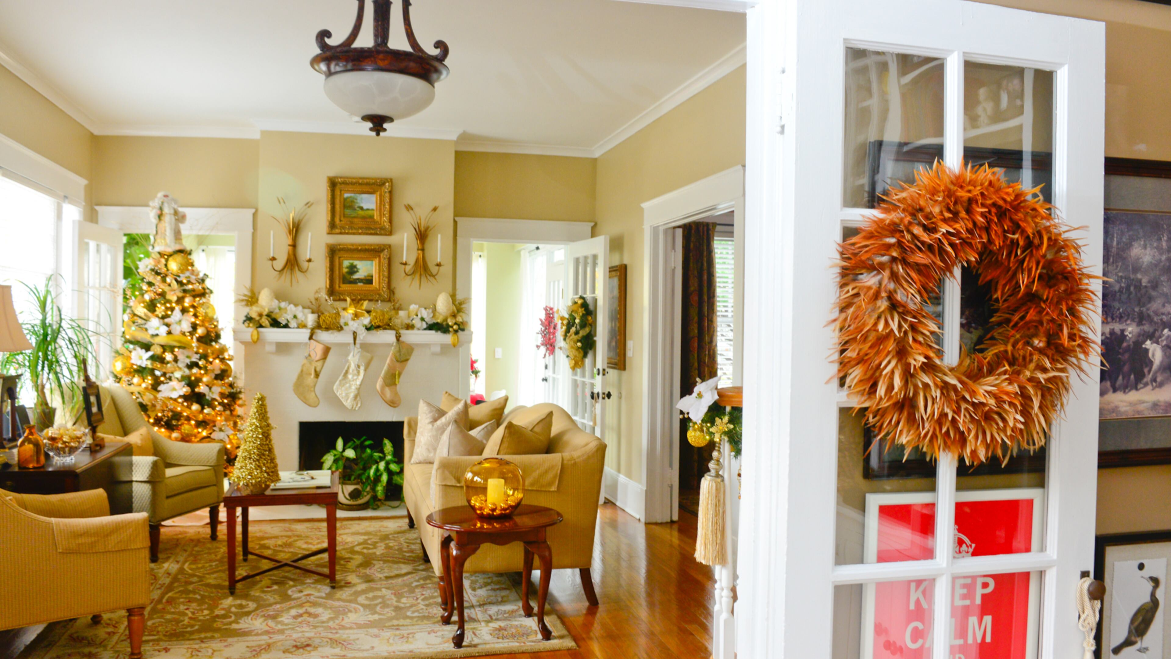 A rustic feather wreath on the door leading to the casual, earth-toned den contrasts with the more formal adjacent living room, which is decorated in bright golds and whites.