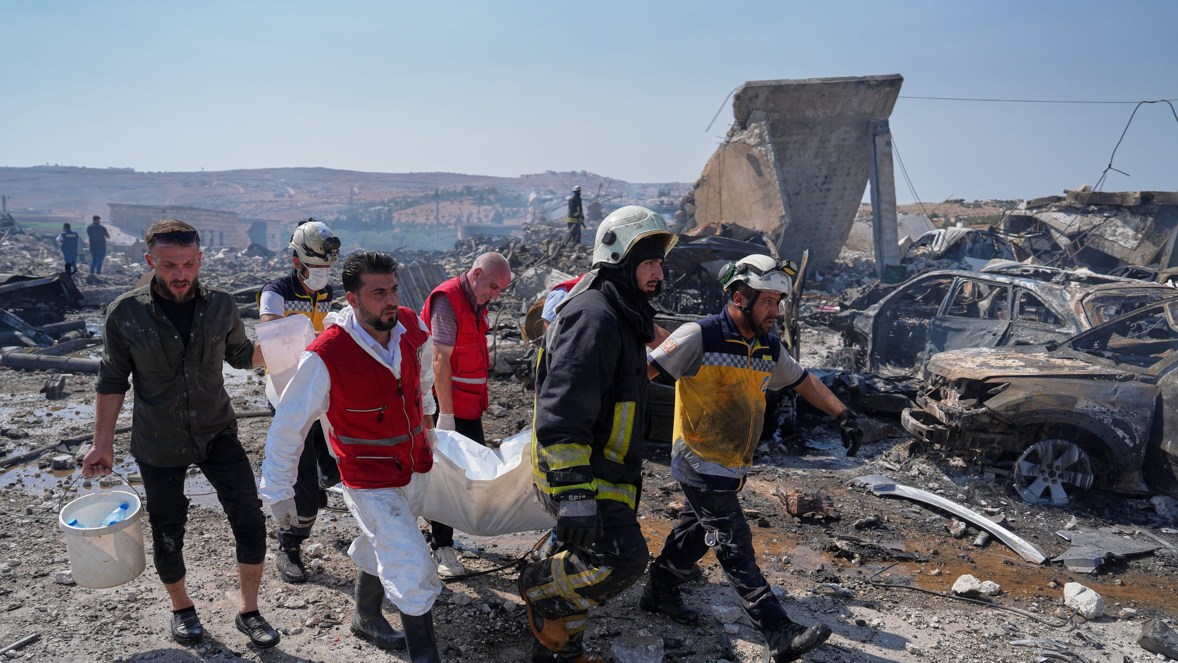 Civil defense workers and a firefighter remove a body from the site of an explosion at what Syria's Defense Ministry said was a warehouse used for the temporary storage of weapons near Sarmada, in Idlib province, Syria, Wednesday, Sept. 9, 2026. (AP Photo/Omar Albam)