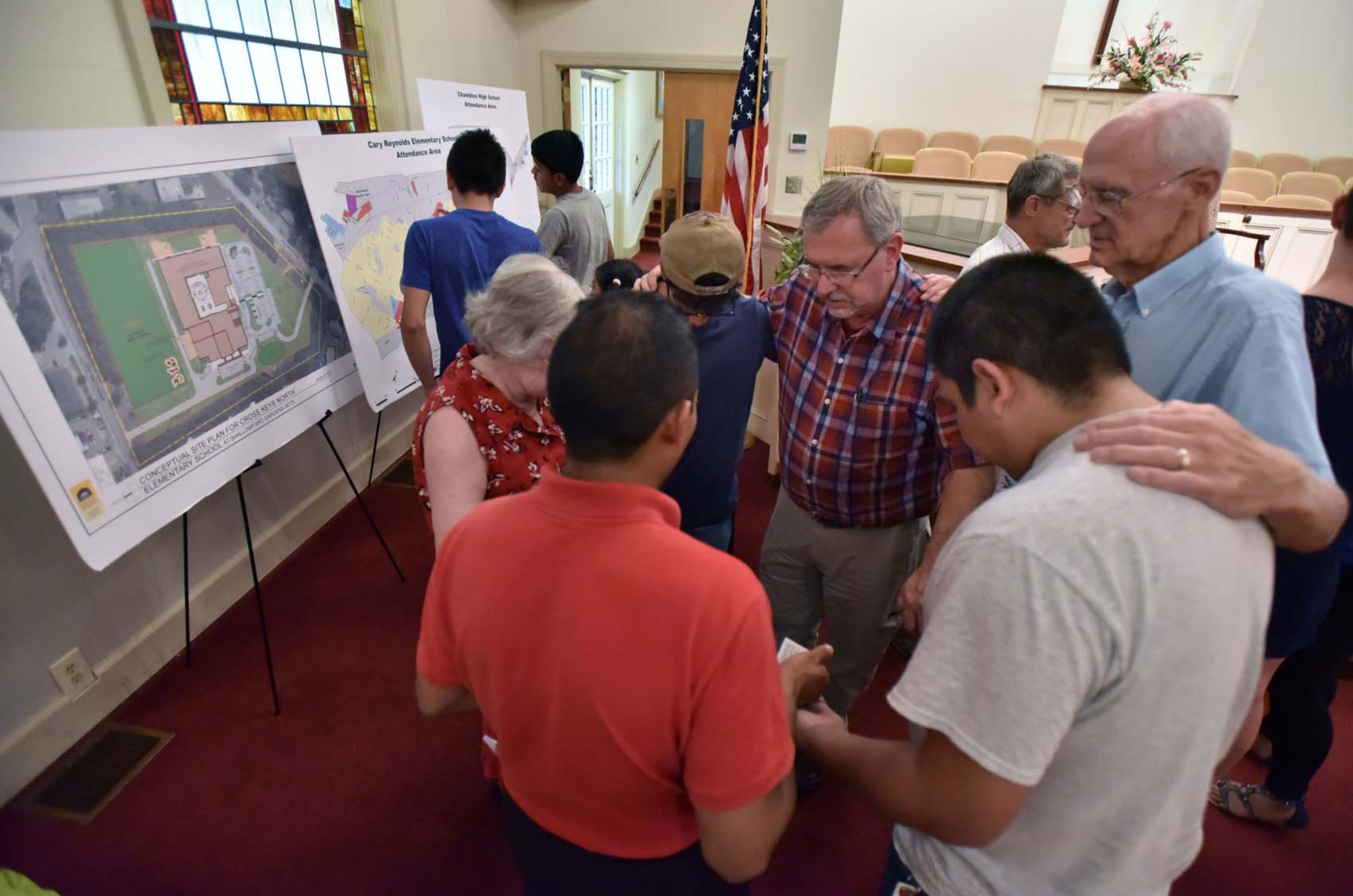 June 14, 2017 Doraville - Pastor Bill Kelly (center) leads a prayer with residents of Shallowford Gardens Apartments after a community meeting with displaced residents at First Baptist Church of Doraville on Wednesday, June 14, 2017. The DeKalb County School District late Monday approved the purchase of a Doraville apartment complex, where they hope to build a new elementary school to alleviate overcrowding in the Cross Keys cluster of schools. The purchase of 3630 Shallowford Road will displace dozens of families in the 104-unit Shallowford Garden Apartments, giving them until the end of August to find new housing. HYOSUB SHIN / HSHIN@AJC.COM
