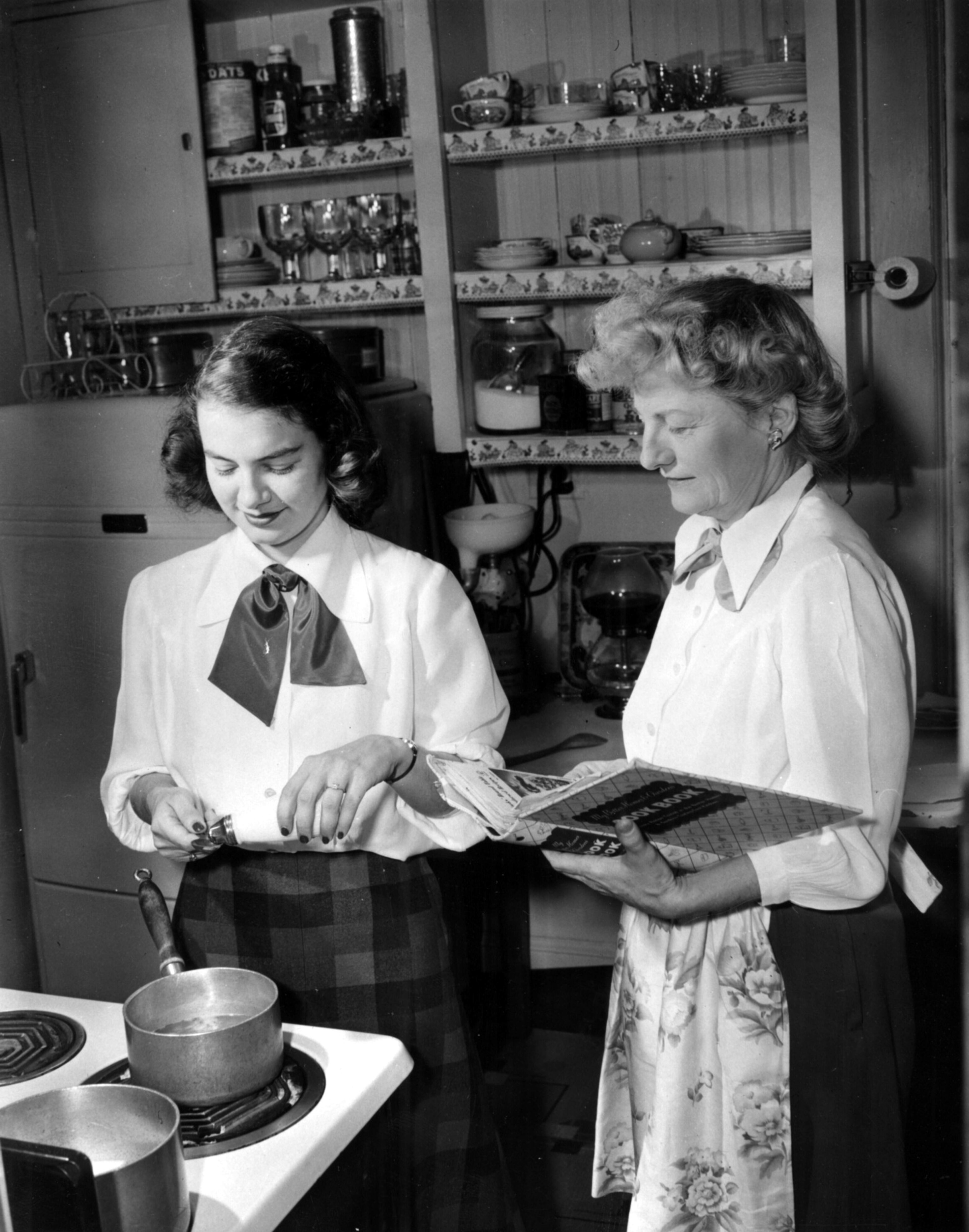 Mrs. C. Douglas Flanigen gives instruction on the art of cooking and use of a cookbook to her daughter Mary, a bride-to-be.