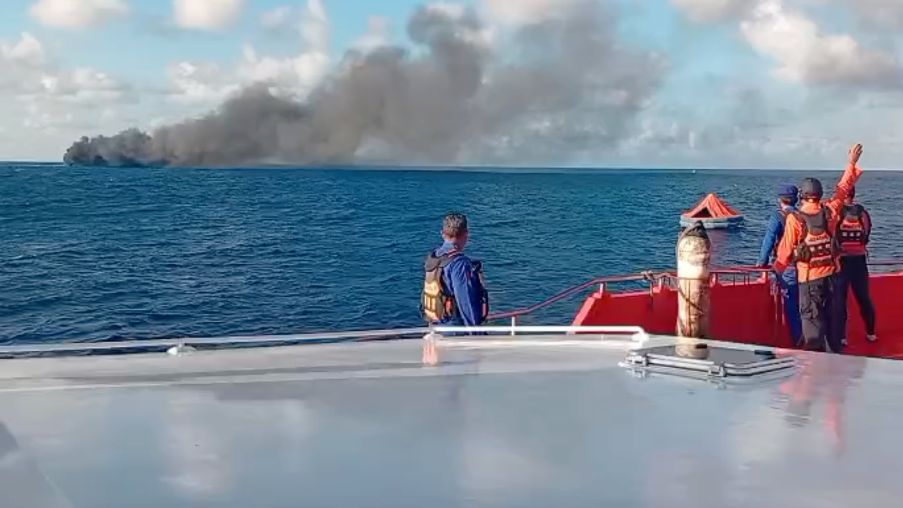 In this image made from video released by the Indonesian National Search and Rescue Agency (BASARNAS), the crew of a rescue ship look on as smoke billows from a passenger ferry that caught fire while traveling from the tourist island of Bali to neighboring island of Lombok, in the waters of Lombok Strait, Indonesia, Wednesday, Aug. 12, 2026. (BASARNAS via AP)