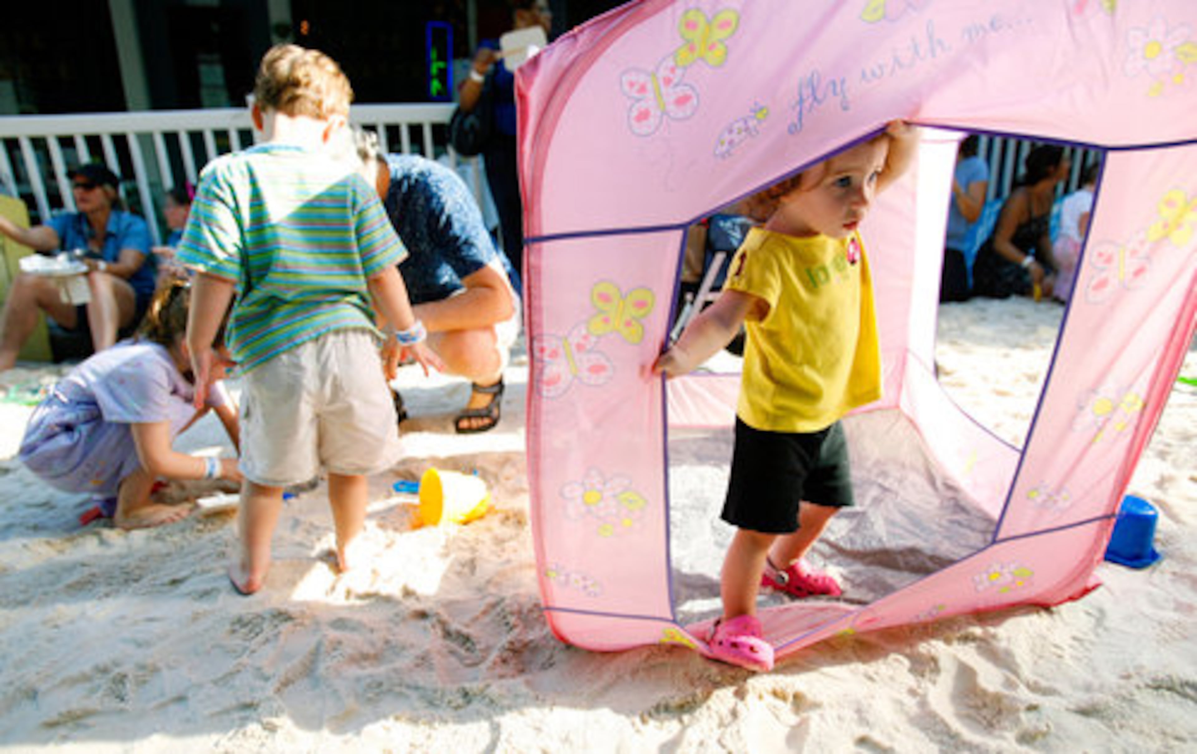 Addison Willis, 1.5 years old, (right) takes shelter in a small playhouse in the sand during the Decatur Beach Party.