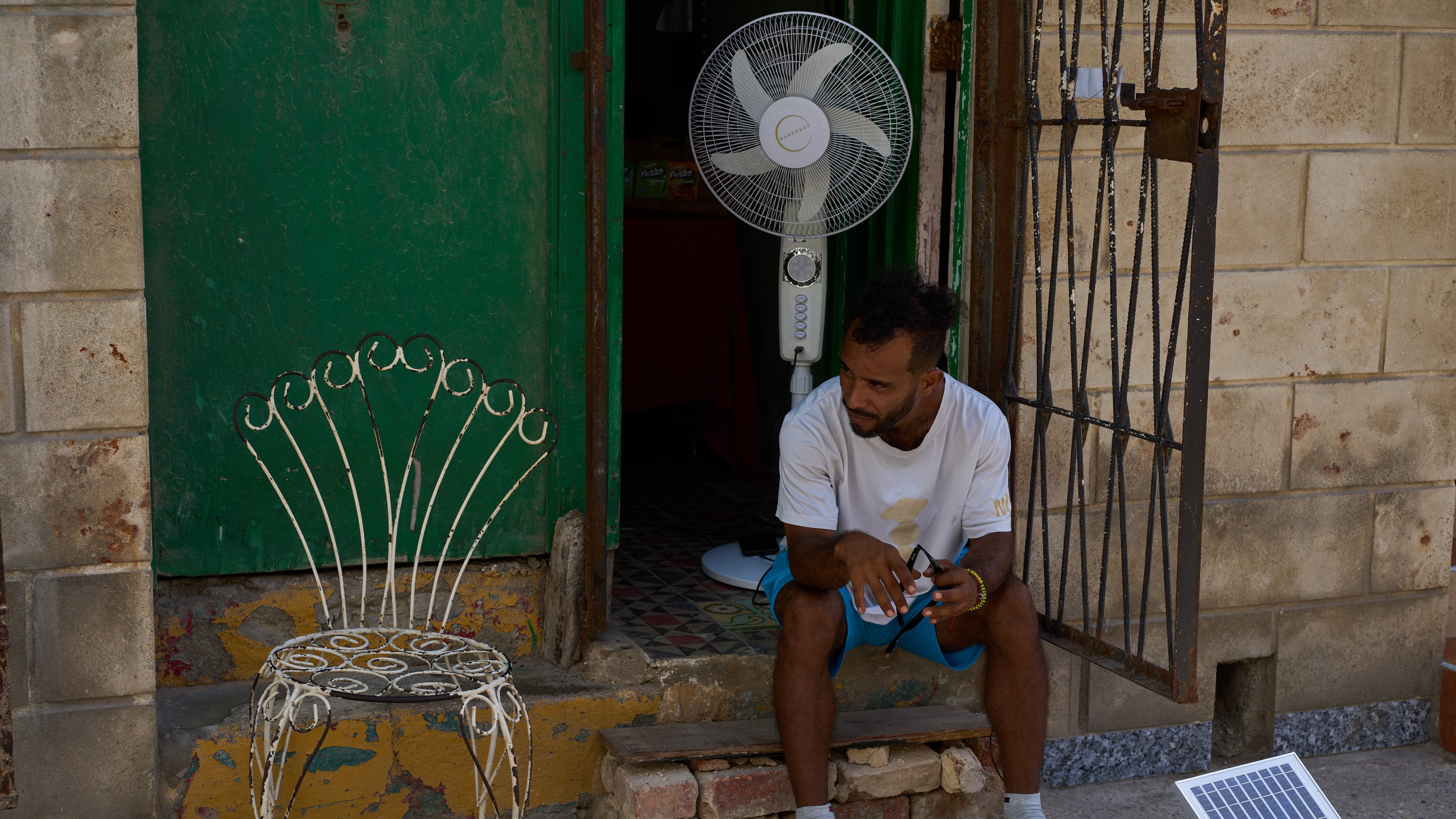A man charges his fan's battery at his doorway using a small solar panel set up on the street during a blackout in Havana, Cuba, Friday, Sept. 18, 2026. (AP Photo/Ramon Espinosa)