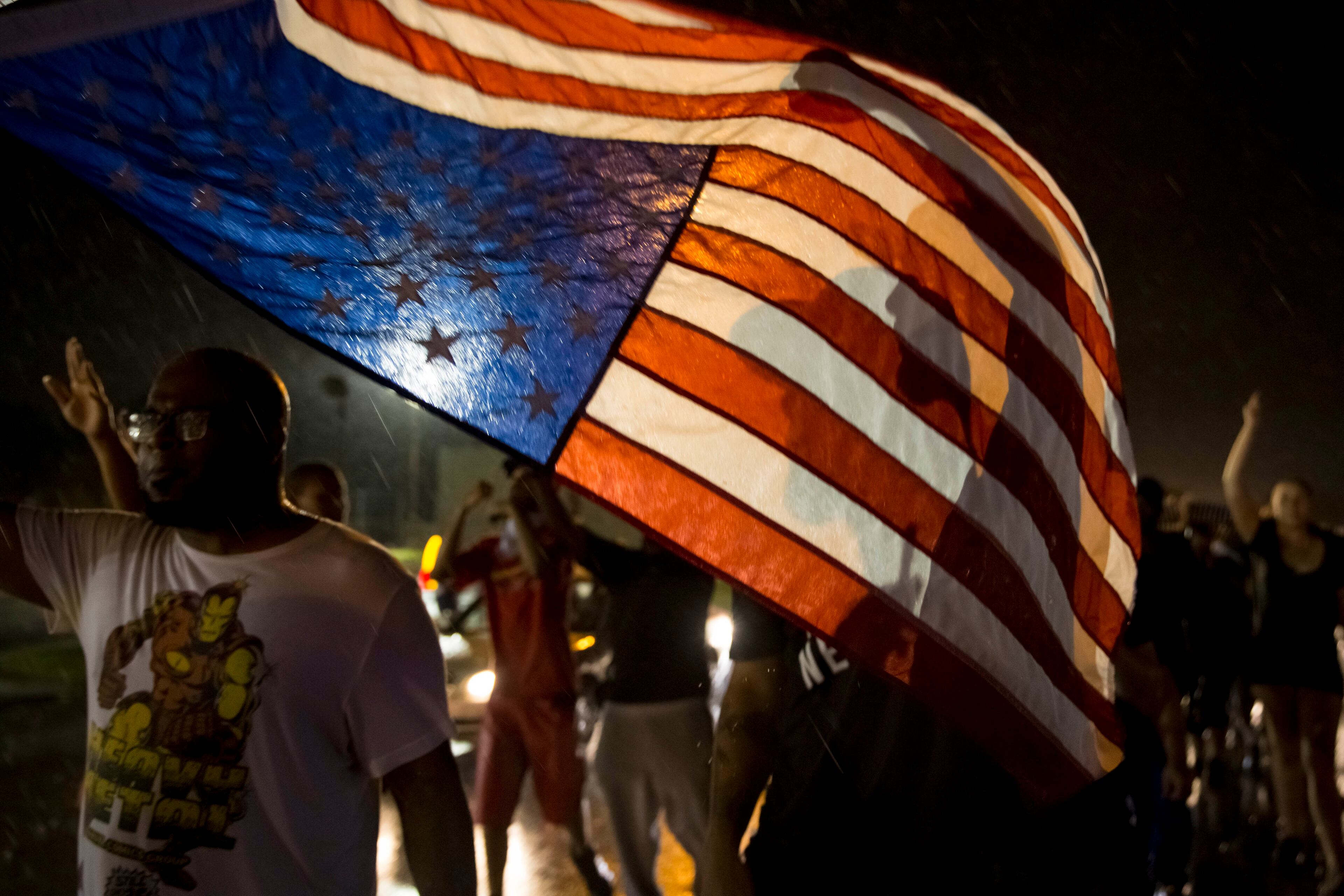 Protesters march down West Florissant Avenue on the anniversary of the fatal shooting of Michael Brown by a police officer in Ferguson, Mo., Aug. 9, 2015. A day of peaceful protest commemorating the killing of an unarmed black teenager by a white police officer one year ago ended in gunfire late Sunday. A St. Louis County police officer was involved in the shooting, the department said. (Whitney Curtis/The New York Times)