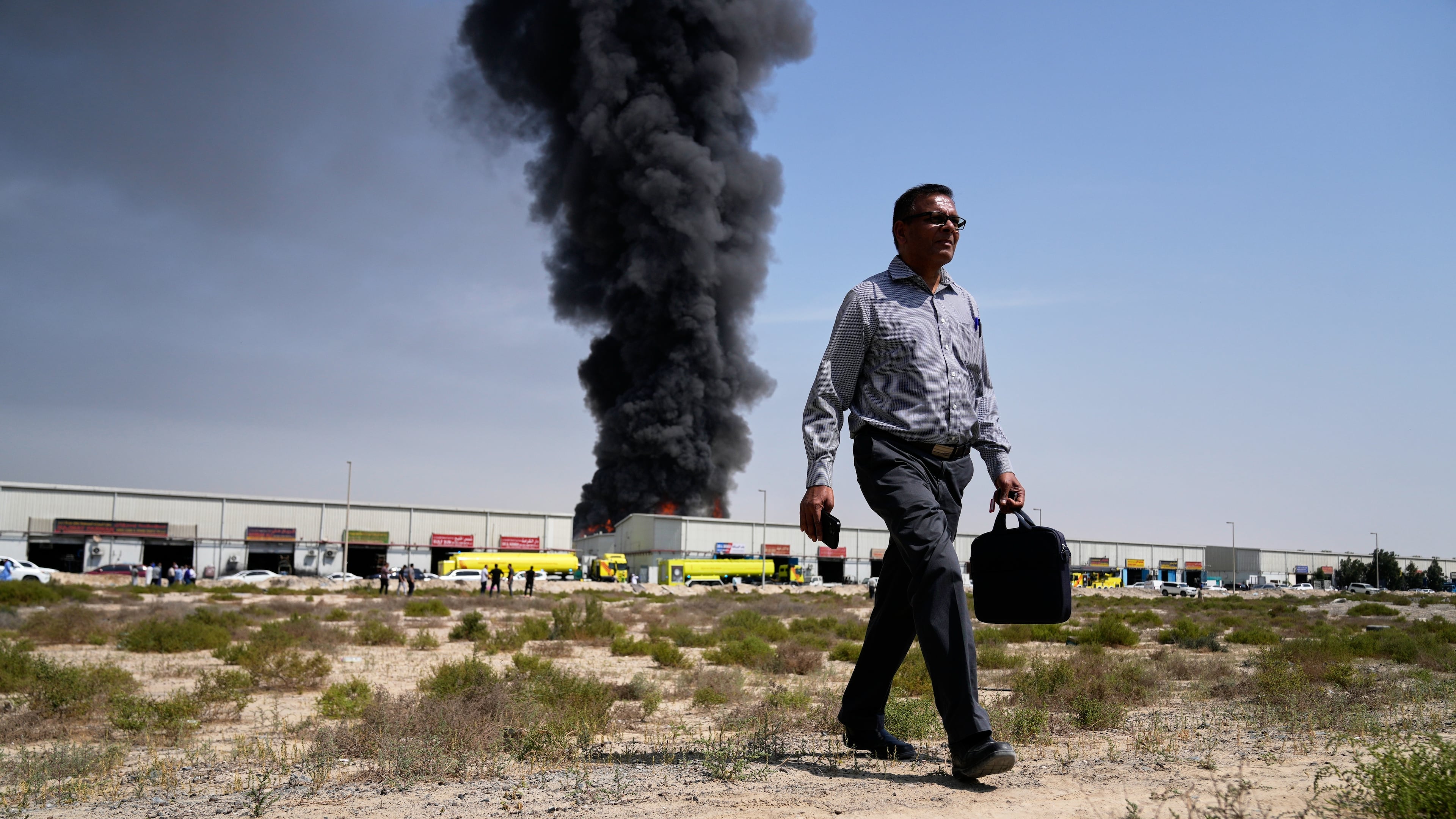 A man walks away after watching as a black plume of smoke rises from a warehouse in the industrial area of Sharjah City, United Arab Emirates, Sunday, March 1, 2026, following reports of Iranian strikes in Dubai. (AP Photo/Altaf Qadri)