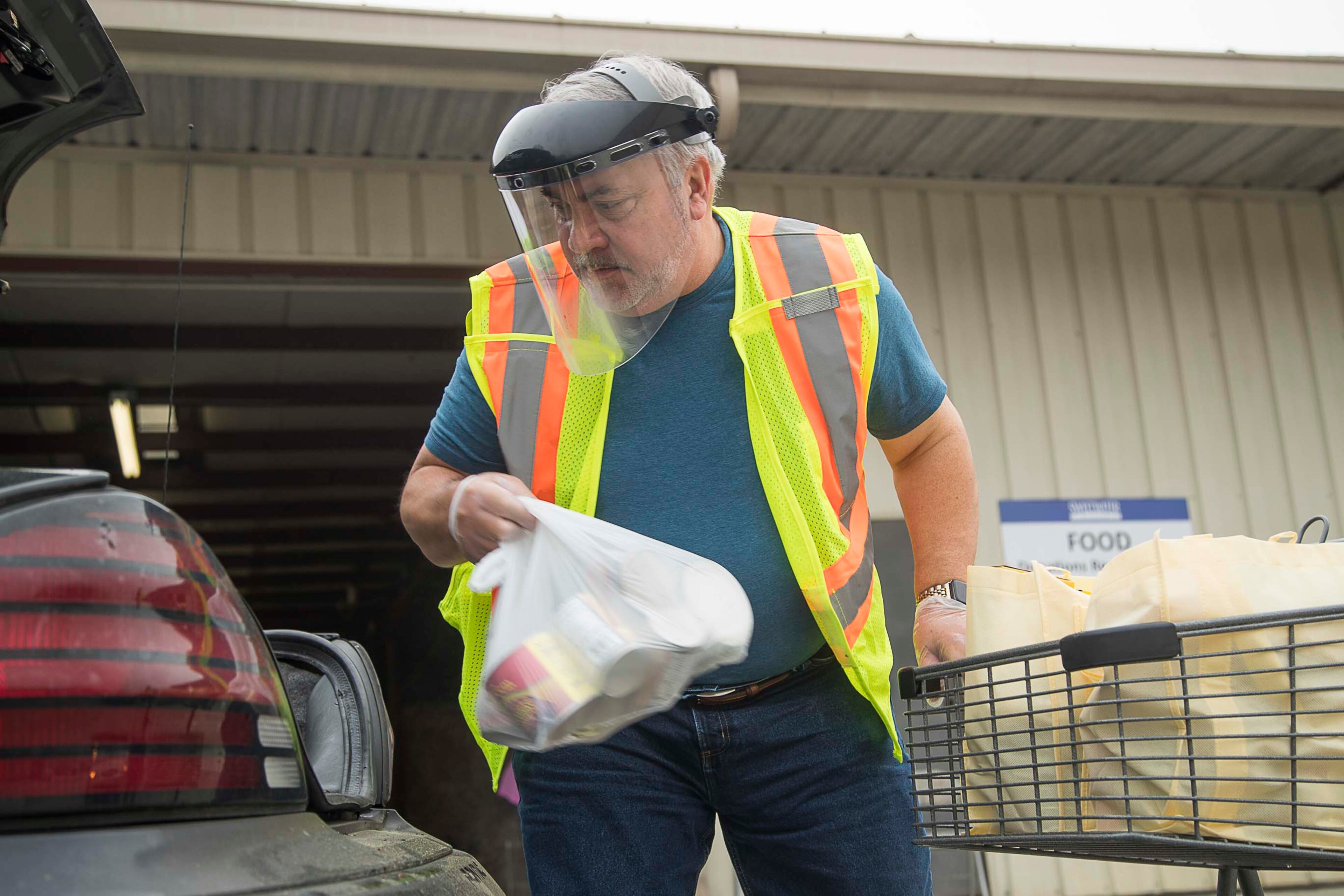 03/19/2020 -- Austell, Georgia -- Sweetwater Mission Executive Director, Brian Hamilton, places pre-bagged groceries inside a patron's vehicle during food distribution "drive-thru" at Sweetwater Mission in Austell, Thursday, March, 19, 2020. Hamilton, along with other volunteers and employees, wore protective wear while facilitating the food distribution. Normally patrons are allowed inside the facility to pick their food but operations have shifted due to coronavirus. (ALYSSA POINTER/ALYSSA.POINTER@AJC.COM)