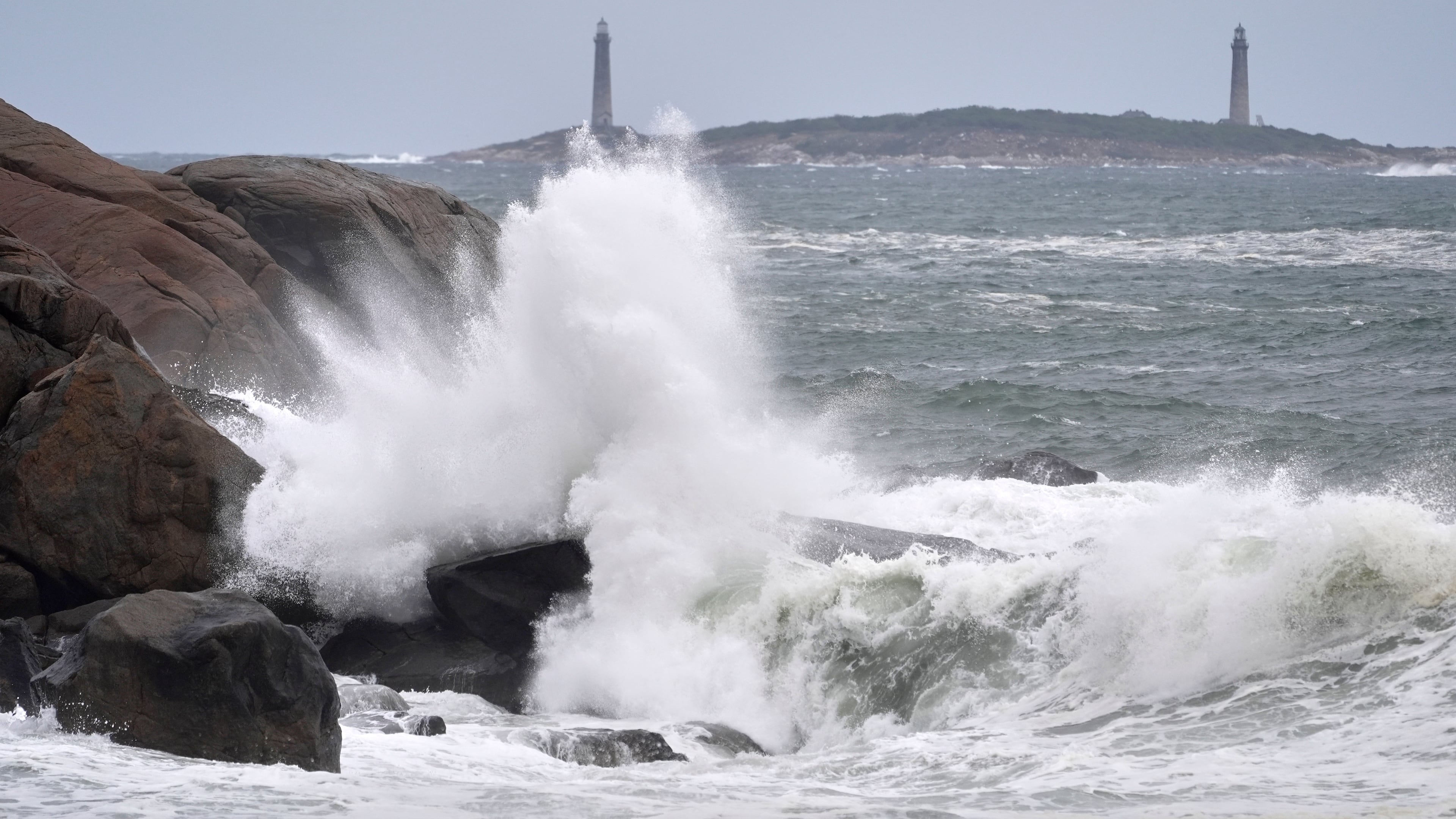 Surf breaks along the rocky coastline, with the twin lighthouses of Thatcher Island visible in the distance, during the early stages of a nor’easter Friday, Sept. 25, 2026, in Gloucester, Mass. (AP Photo/Robert F. Bukaty)