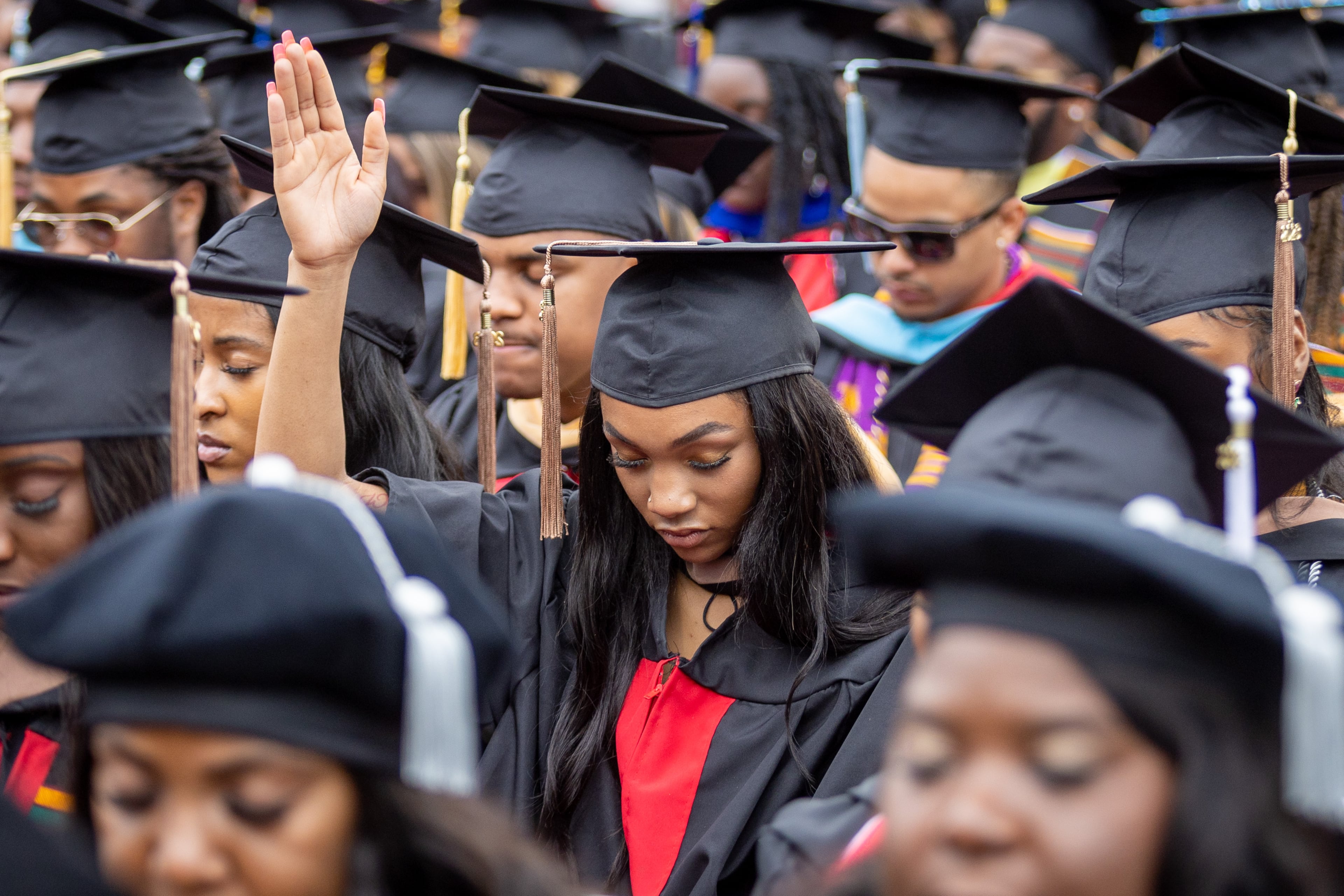 Graduates bow their heads in prayer at the beginning of Clark Atlanta University's commencement ceremony in Panther Stadium on Saturday, May 20, 2023. (Steve Schaefer / steve.schaefer@ajc.com)