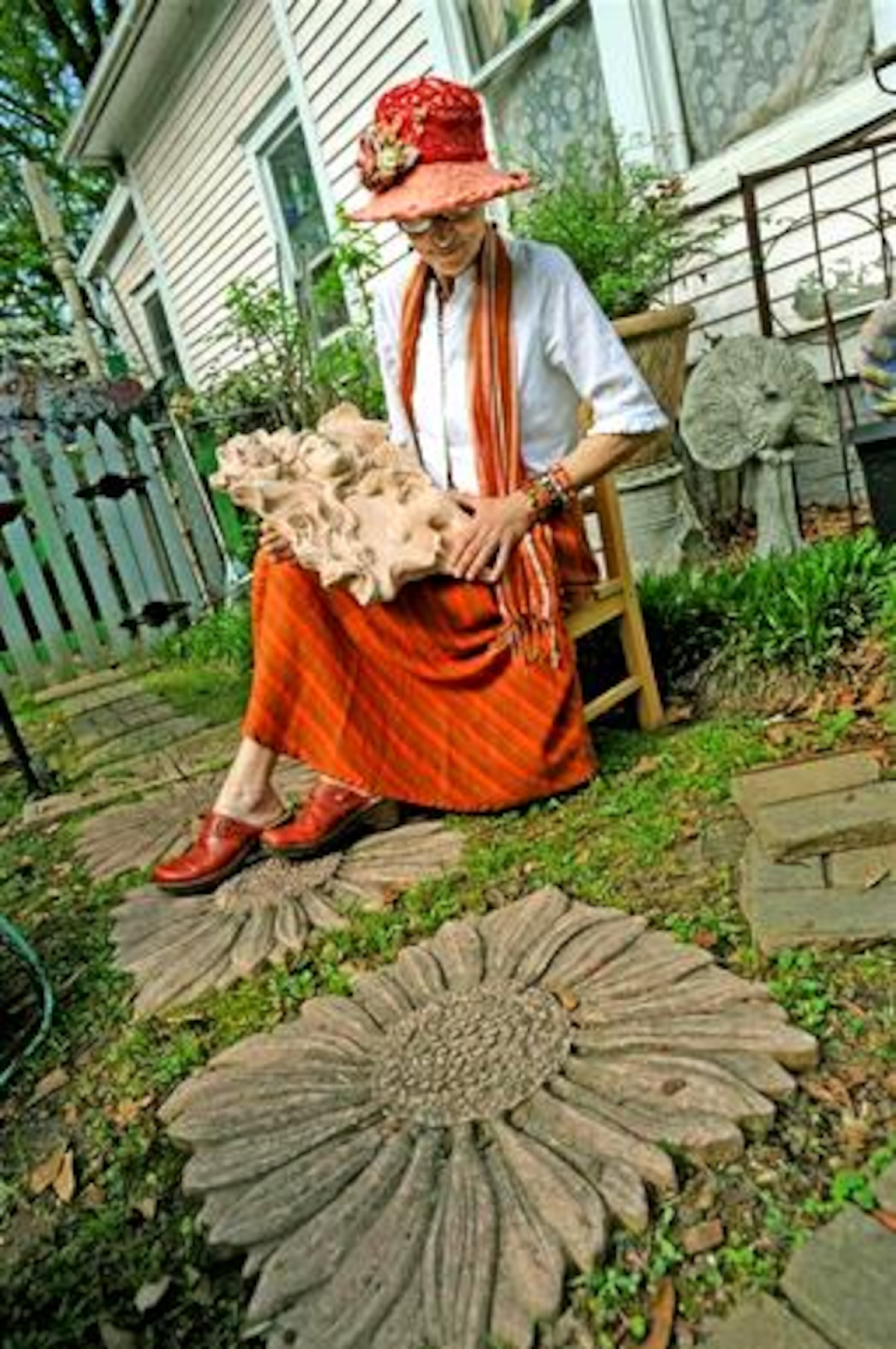 Angela Carrington, a longtime friend of local artist Christine Sibley, holds one of her concrete pieces, while large sunflower stepping stones form a path.