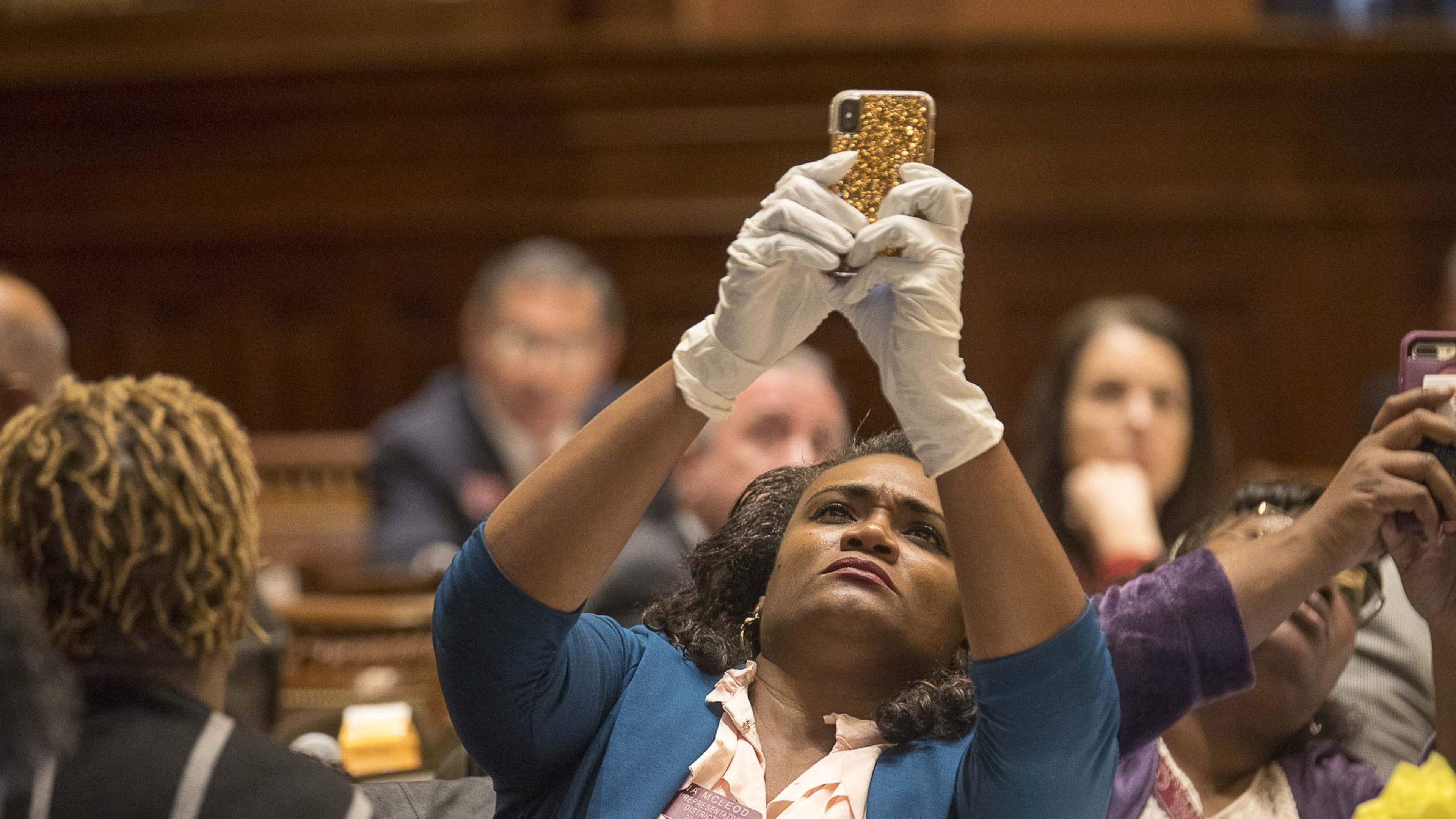 Georgia Rep. Donna McLeod, D - Lawrenceville, takes a photo of the final vote on the House resolution while wearing gloves during a special called session at the Georgia State Capitol Building, Monday, March 16, 2020. (ALYSSA POINTER/ALYSSA.POINTER@AJC.COM)
