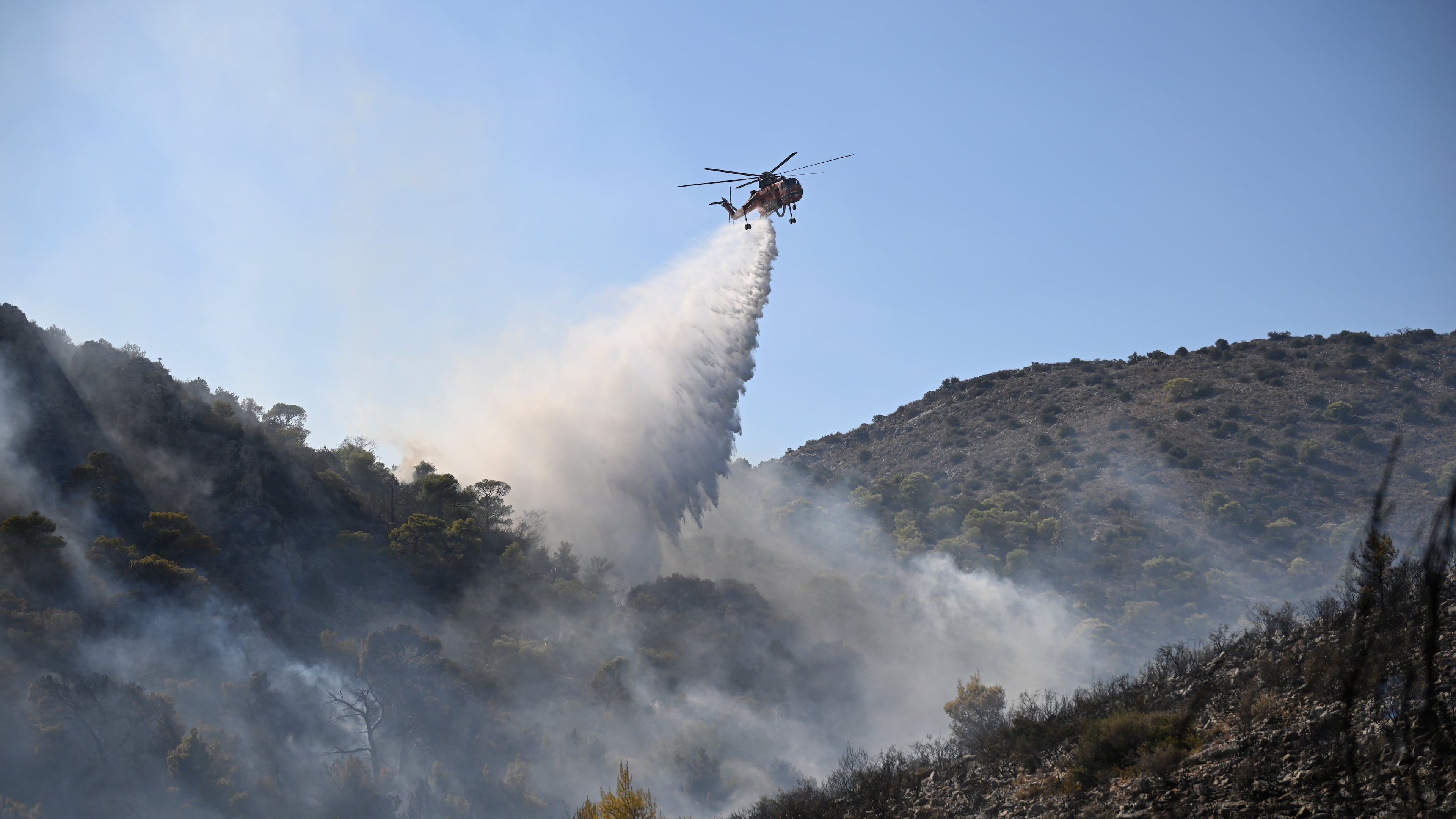 A helicopter drops water on a wildfire on the island of Salamina, west of Athens, Greece, Sunday, Aug. 16, 2026. (AP Photo/Michael Varaklas)