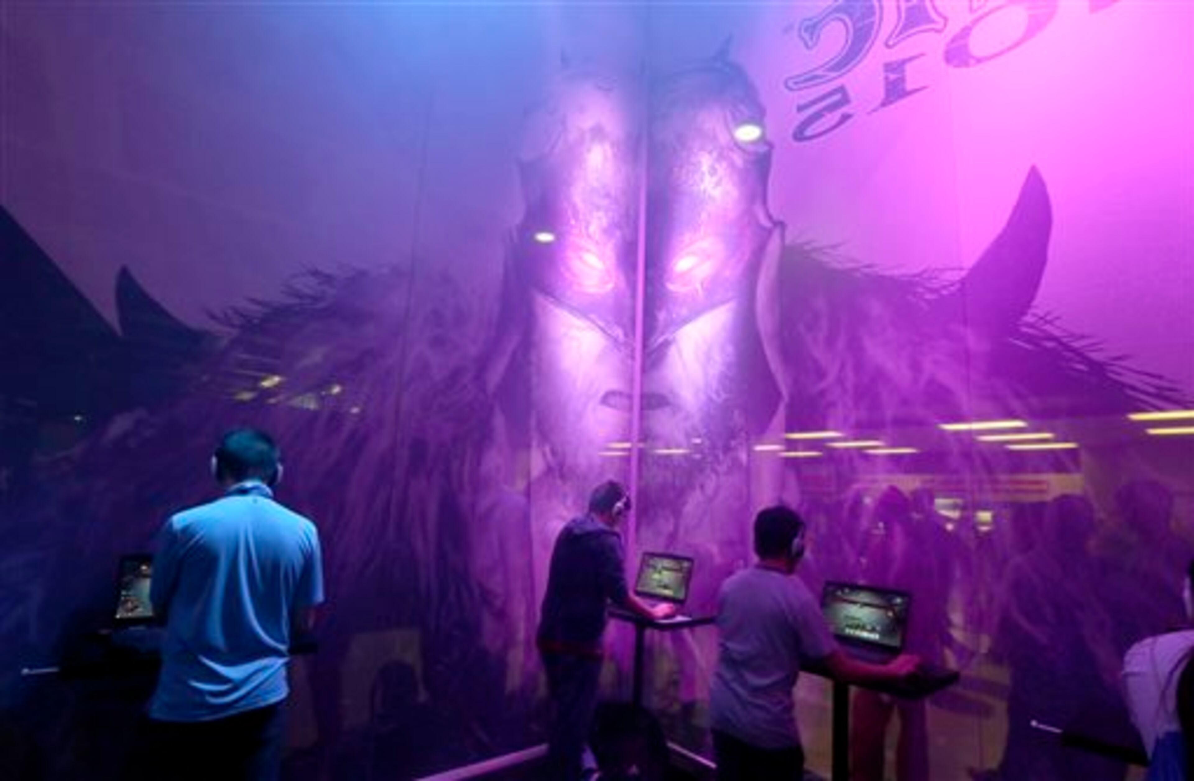 A masked character looms over video gamers playing Magic 2015 - Duels of the Planeswalkers from Wizards of the Coast, Friday, Aug. 29, 2014, in a booth at the Penny Arcade Expo, a fan-centric celebration of gaming in Seattle. The event is expected to be attended by roughly 85,000 gamers and will include concerts, game tournaments and previews of upcoming titles. (AP Photo/Ted S. Warren)