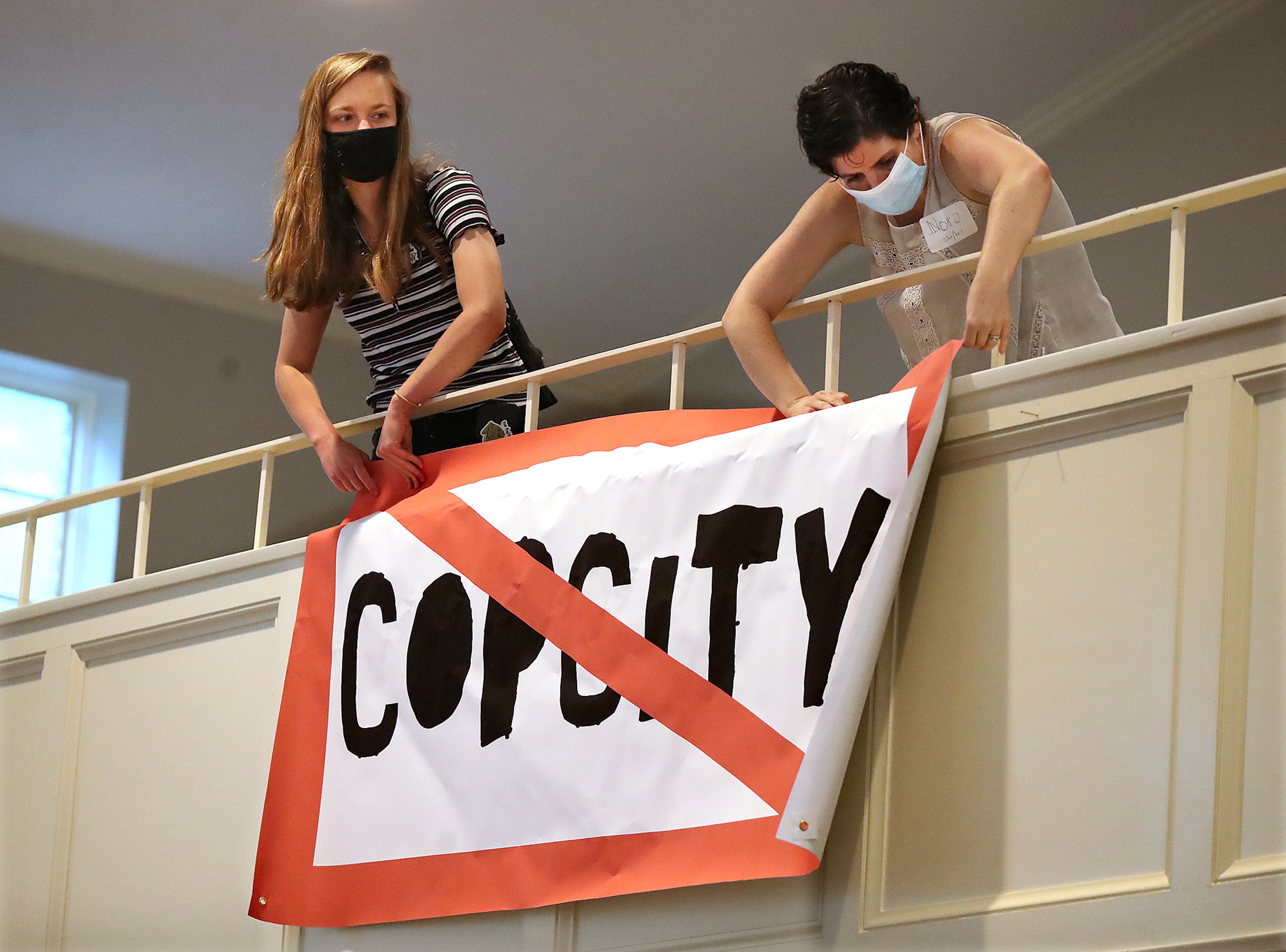 080521 Atlanta: Local activists Kelsea (left) and Nora (right), who go by first names only, hang a "Stop Cop City" banner from the balcony of the Neighborhood Church during a town hall meeting to gather public input in opposition to the plans for a new police and fire training facility in DeKalb County on Thursday, August 5, 2021, in Atlanta. “Curtis Compton / Curtis.Compton@ajc.com”