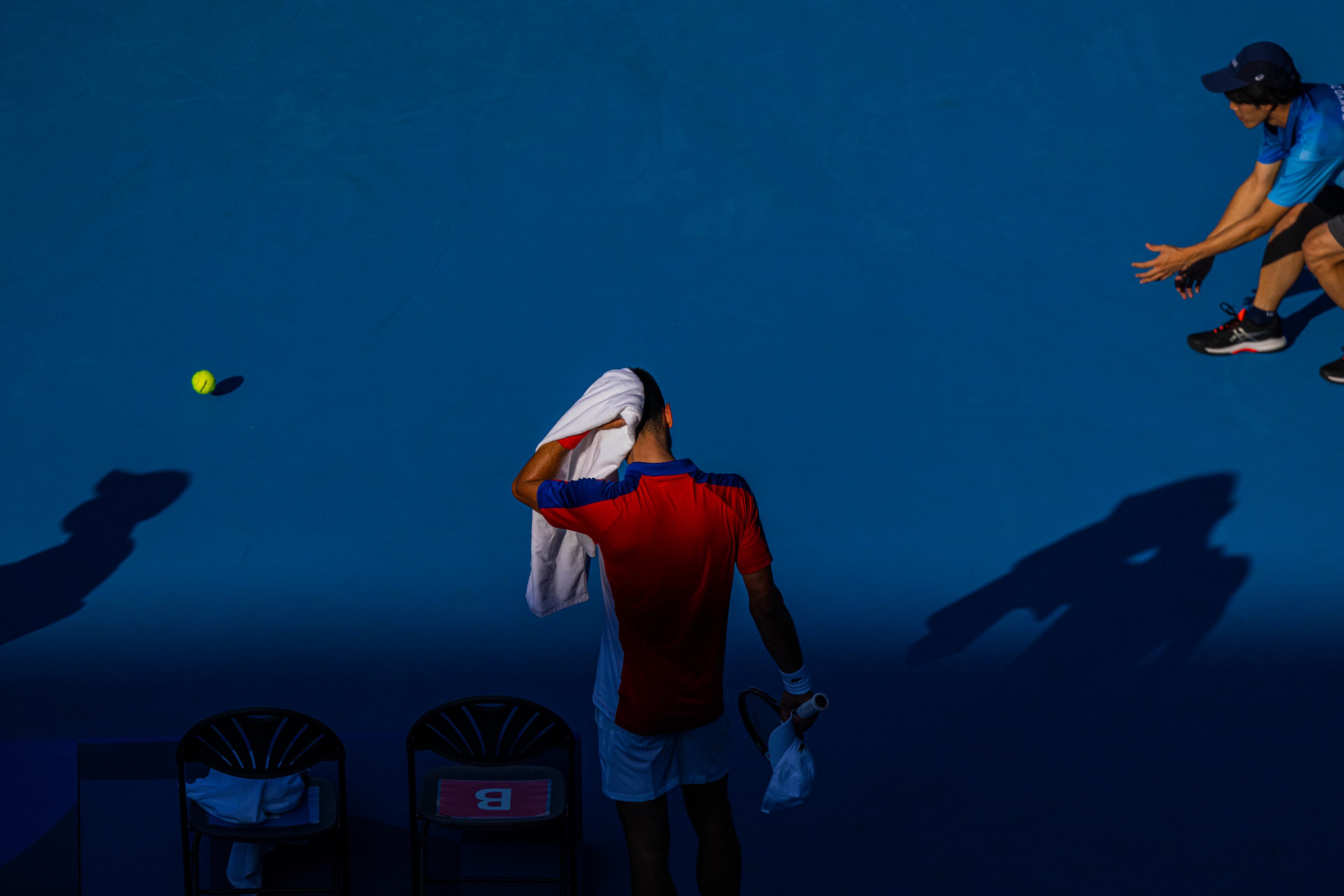 Novak Djokovic of Serbia uses a towel to wipe his head during his match against Hugo Dellien of Bolivia at the postponed 2020 Tokyo Olympics in Tokyo on July 24, 2021. An unusual Olympics is missing the atmosphere fans bring to events. What is left is not silence, but something else.(Hiroko Masuike/The New York Times)