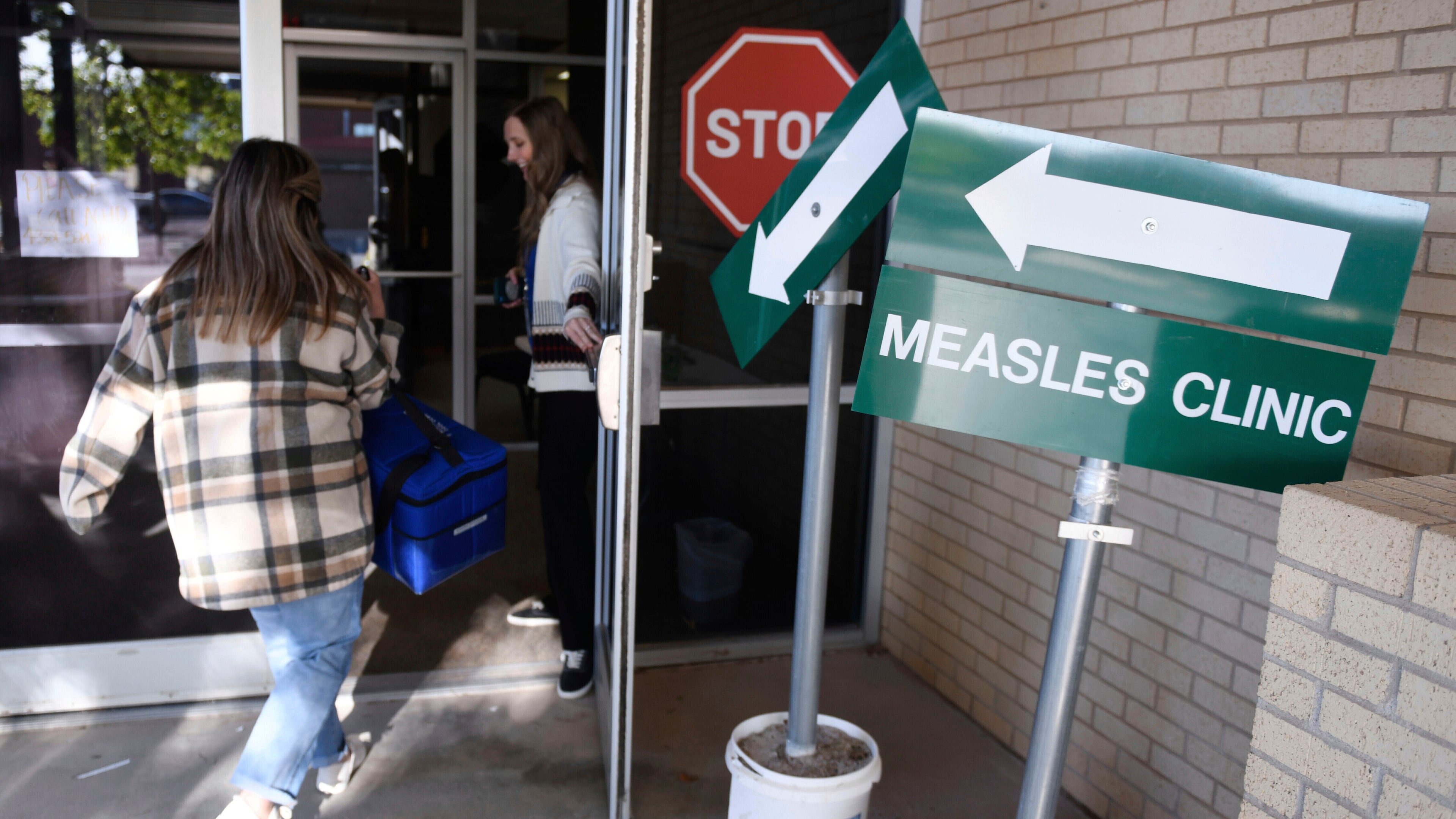 FILE - Health department staff members enter the Andrews County Health Department measles clinic carrying doses of the measles, mumps and rubella vaccine, April 8, 2025, in Andrews, Texas. (AP Photo/Annie Rice, File)