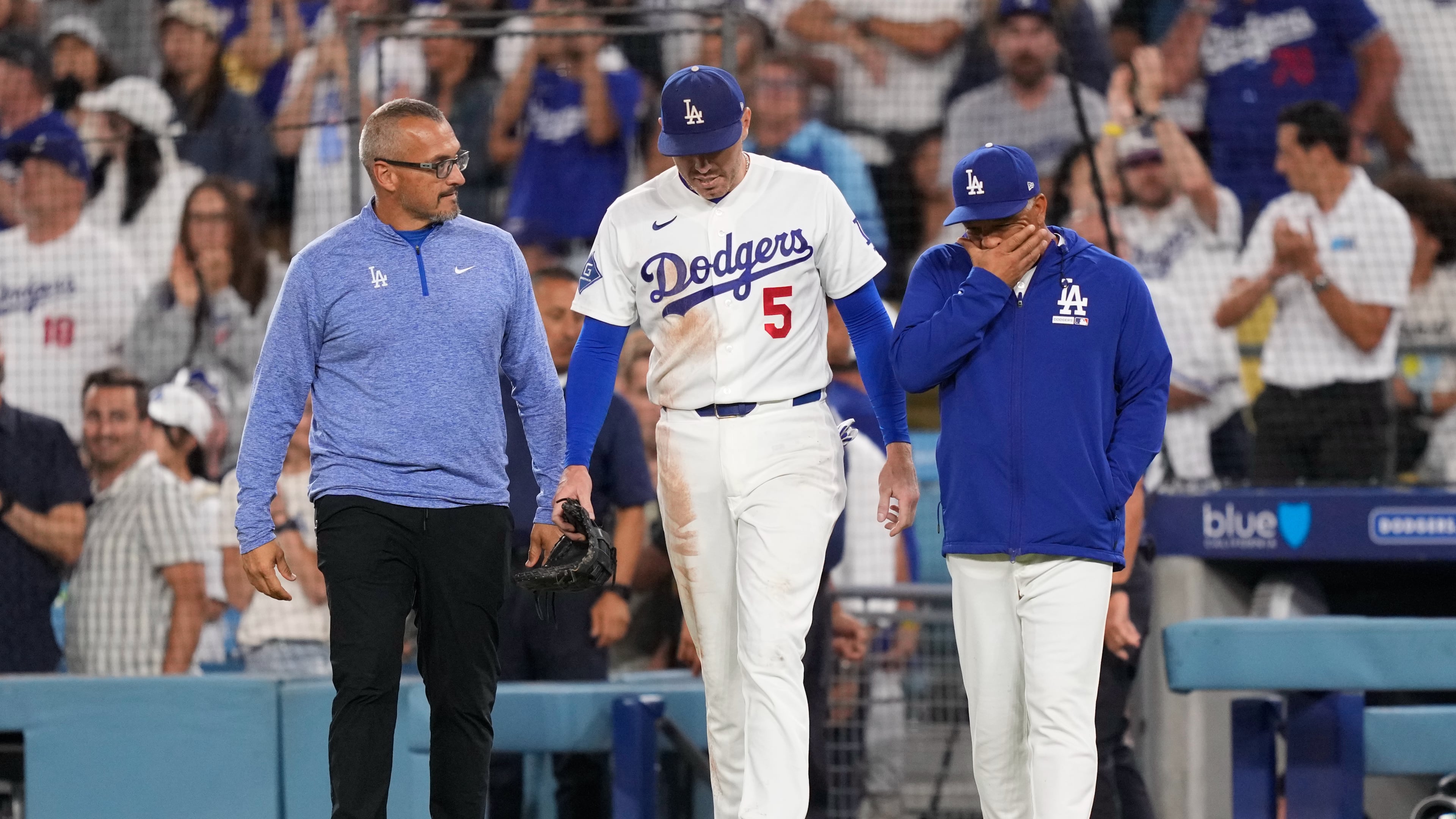 Los Angeles Dodgers first baseman Freddie Freeman, center, walks back on to the field accompanied by manager Dave Roberts, right, and trainer Greg Barajas after he fell into the dugout while trying to catch a foul ball hit by Kansas City Royals' Isaac Collins during the eighth inning of a baseball game Wednesday, Aug. 12, 2026, in Los Angeles. (AP Photo/Mark J. Terrill)