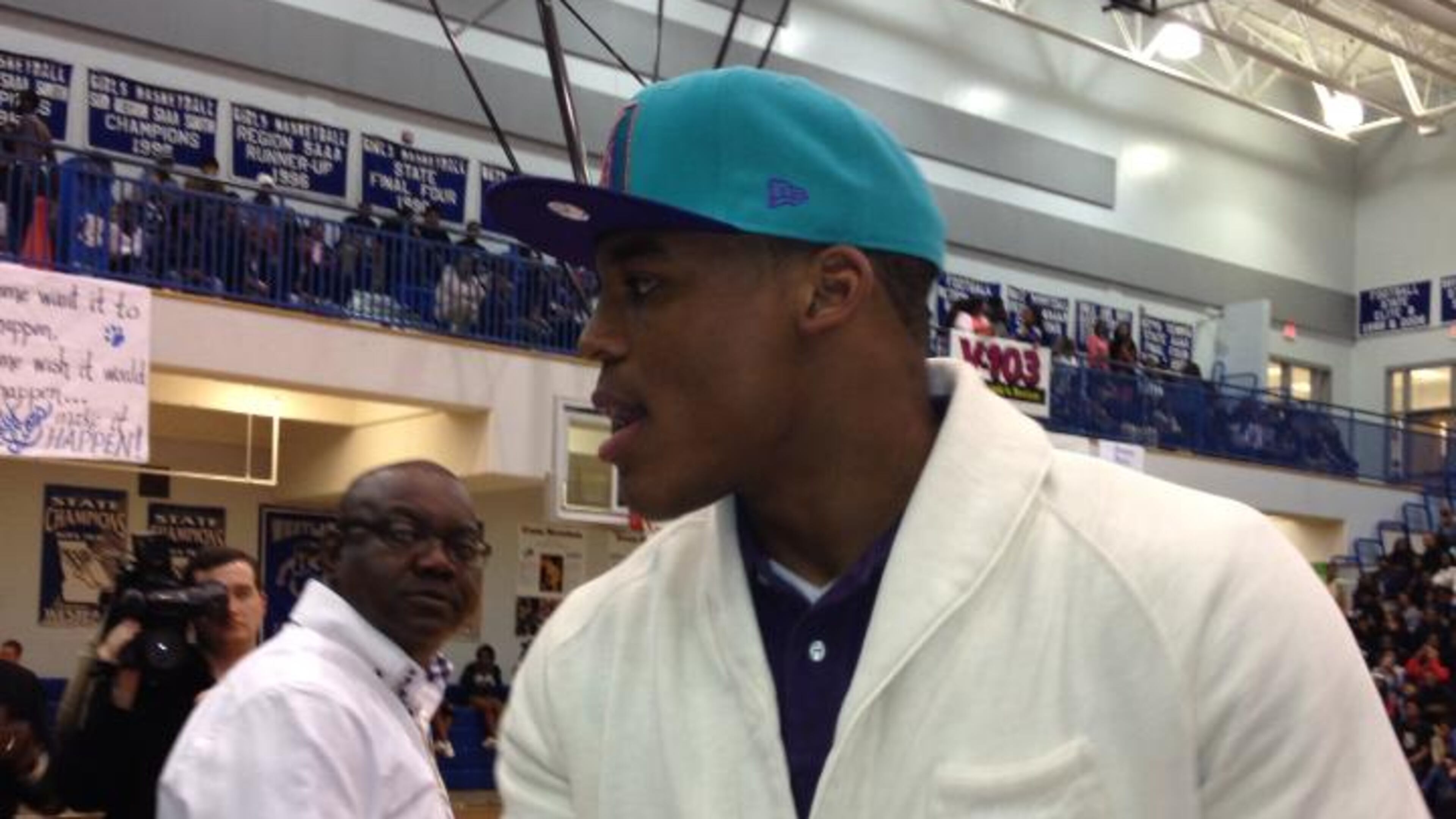 Cam Newton shakes the official scorer's had before his jersey is retired. His former coach, Dallas Allen, is in the background.