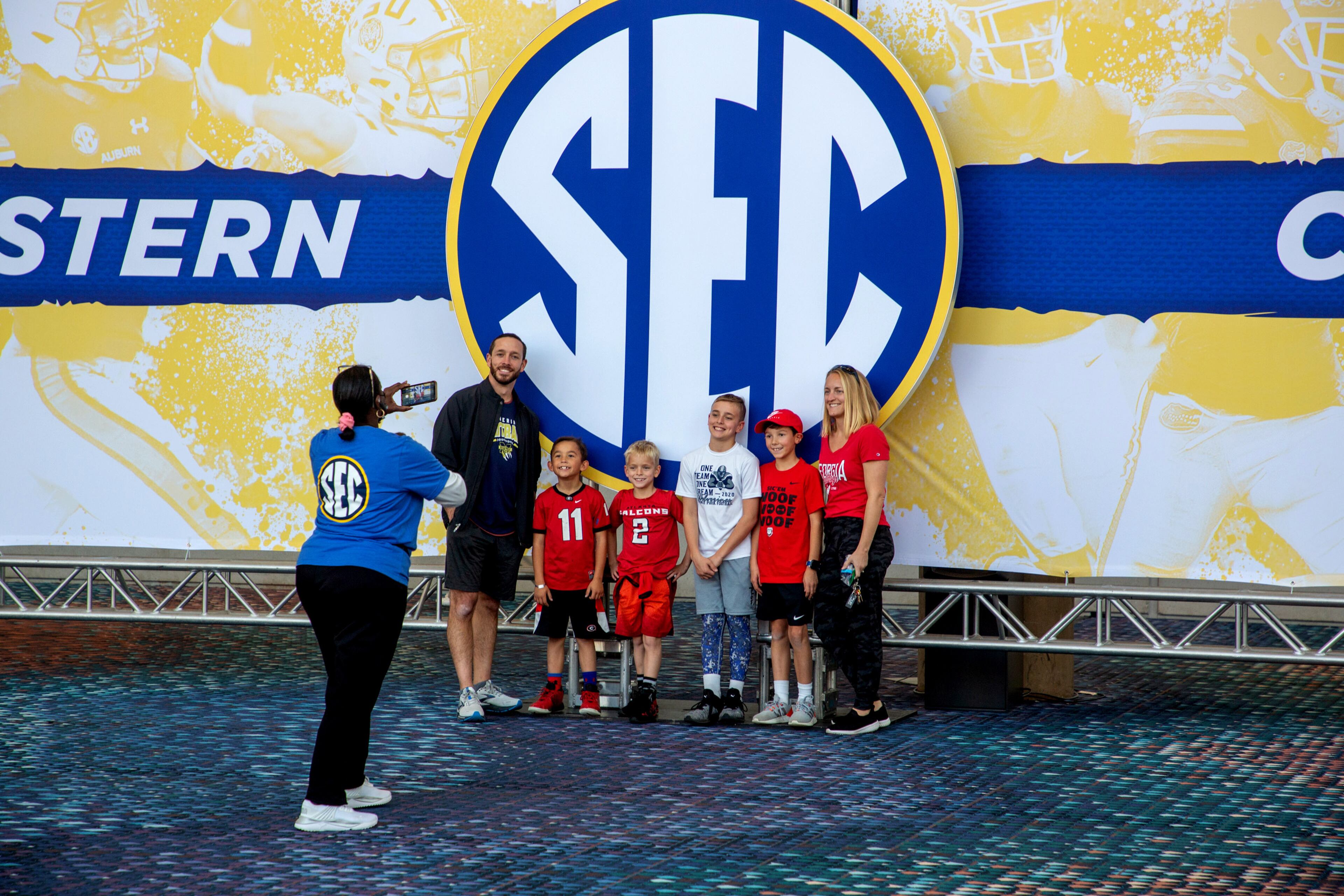 Volunteer Penny Mitchell (L) takes a picture of a family in front of the large SEC sign as they had to the SEC fanfare in the World Congress Center on Friday, November 3, 2021. STEVE SCHAEFER FOR THE ATLANTA