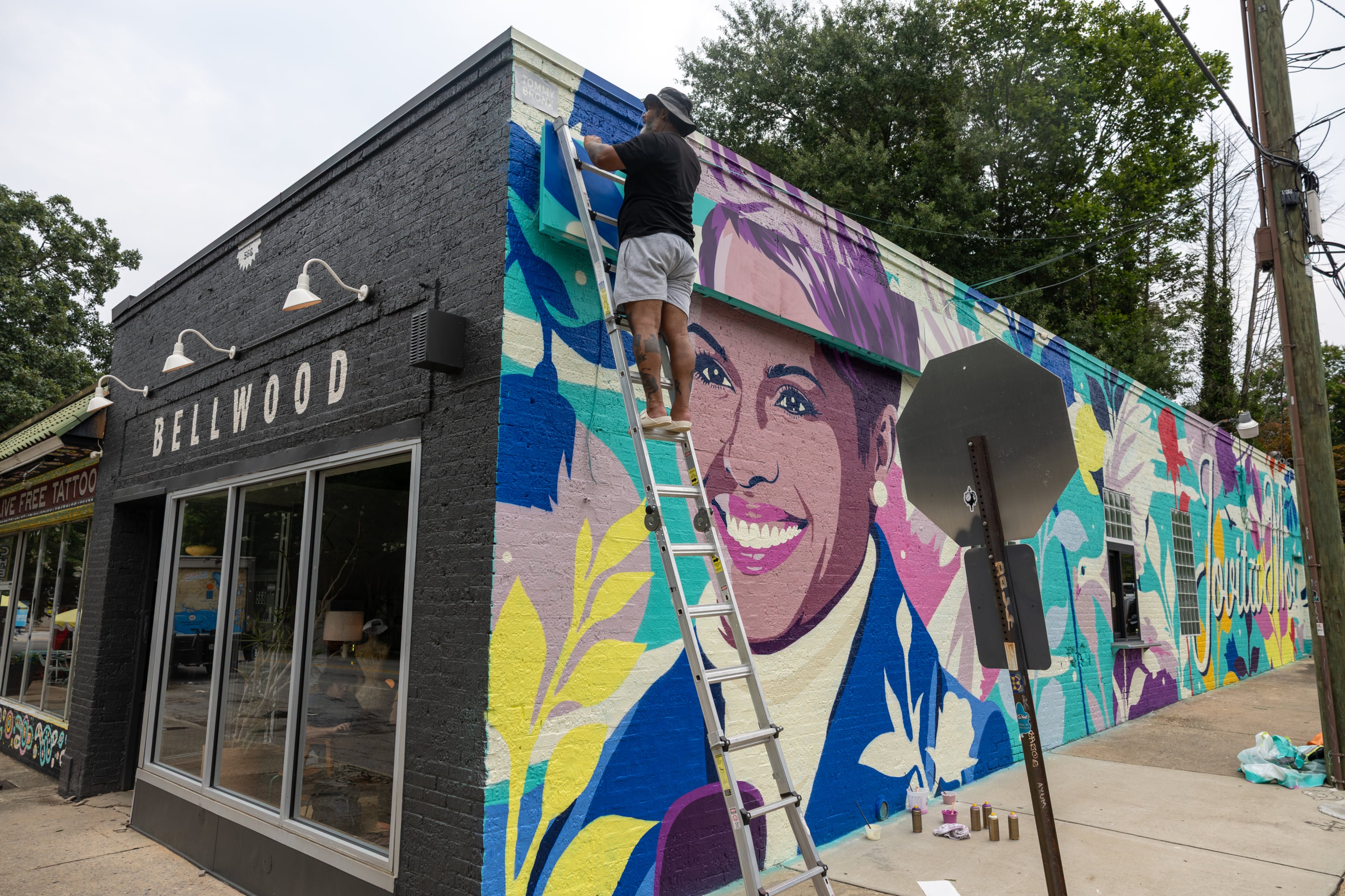 Artist Tommy Bronx (top) puts finishing touches on his new mural honoring the late news anchor Jovita Moore on the side of Bellwood Coffee in Atlanta on July 29, 2026. The coffee shop created community outcry when it painted over the original mural of Moore. (Arvin Temkar/AJC)