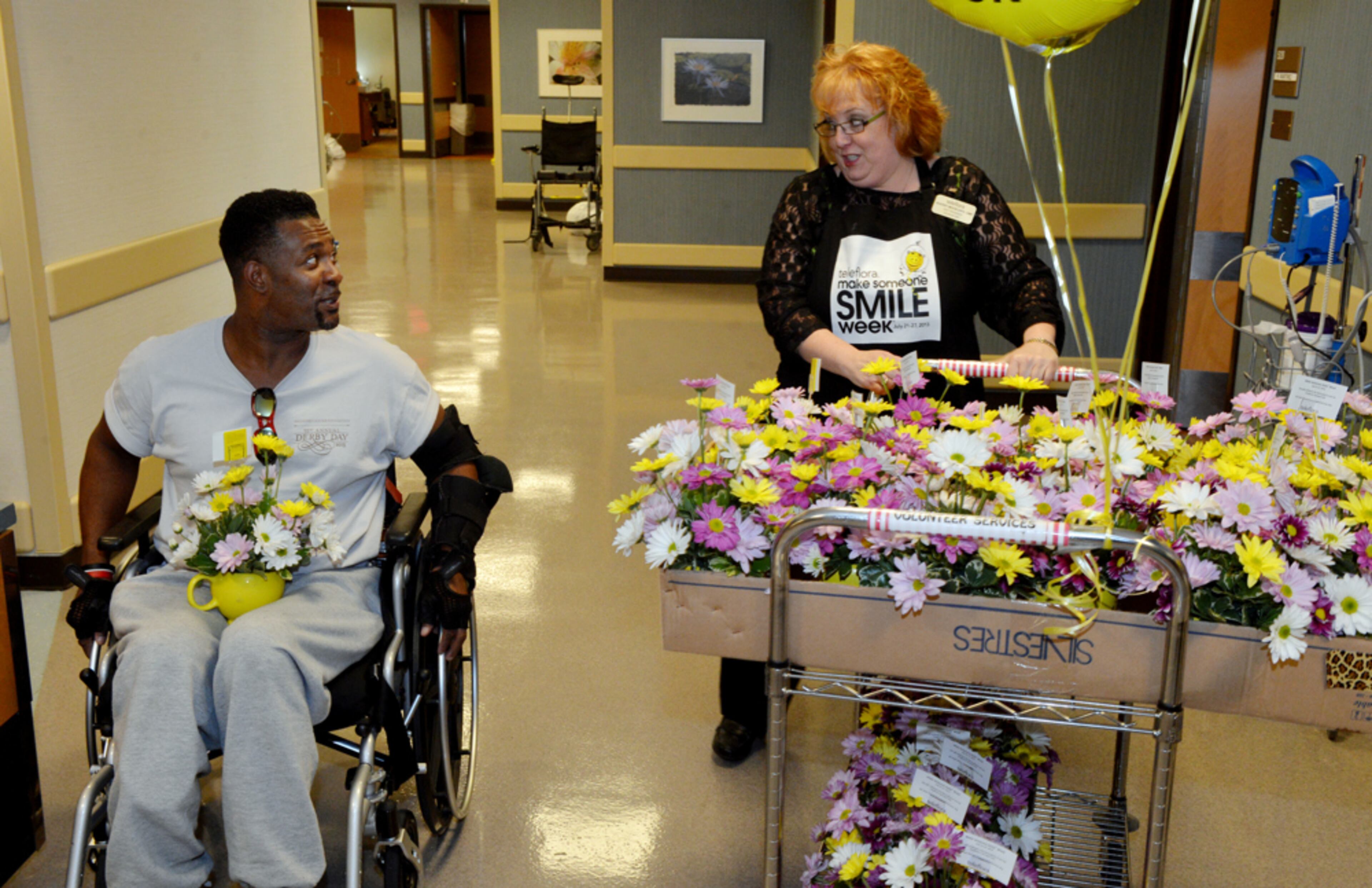 LEDE JULY 23, 2013 ATLANTA Sheldon Thomas of Fairburn talks with Sherry Moon as she delivers flowers Tuesday. Local Atlanta florist, Sherry Moon, owner of Buckhead Wright's Florist and hospital staff deliver flowers at the Shepherd Center Tuesday July 23, for Make Someone Smile Week, the floral industry's leading benevolent program. Sherry along with other local florists and volunteers surprised 150 patients at the Shepherd Spinal Center with Be Happy Bouquets filled with bright flowers compliments of Teleflora and Buckhead Wright's Florist. Each florist who participates selects the facility and Sherry chose Shepherd because of the care her nephew received when he was a patient. KENT D. JOHNSON / KDJOHNSON@AJC.COM I try to cover these type of events because it shows our readers that even in adversity, there can be smiles. Made with NIKON D4, 38mm, f/9, 1/60 sec, 2000 ISO.