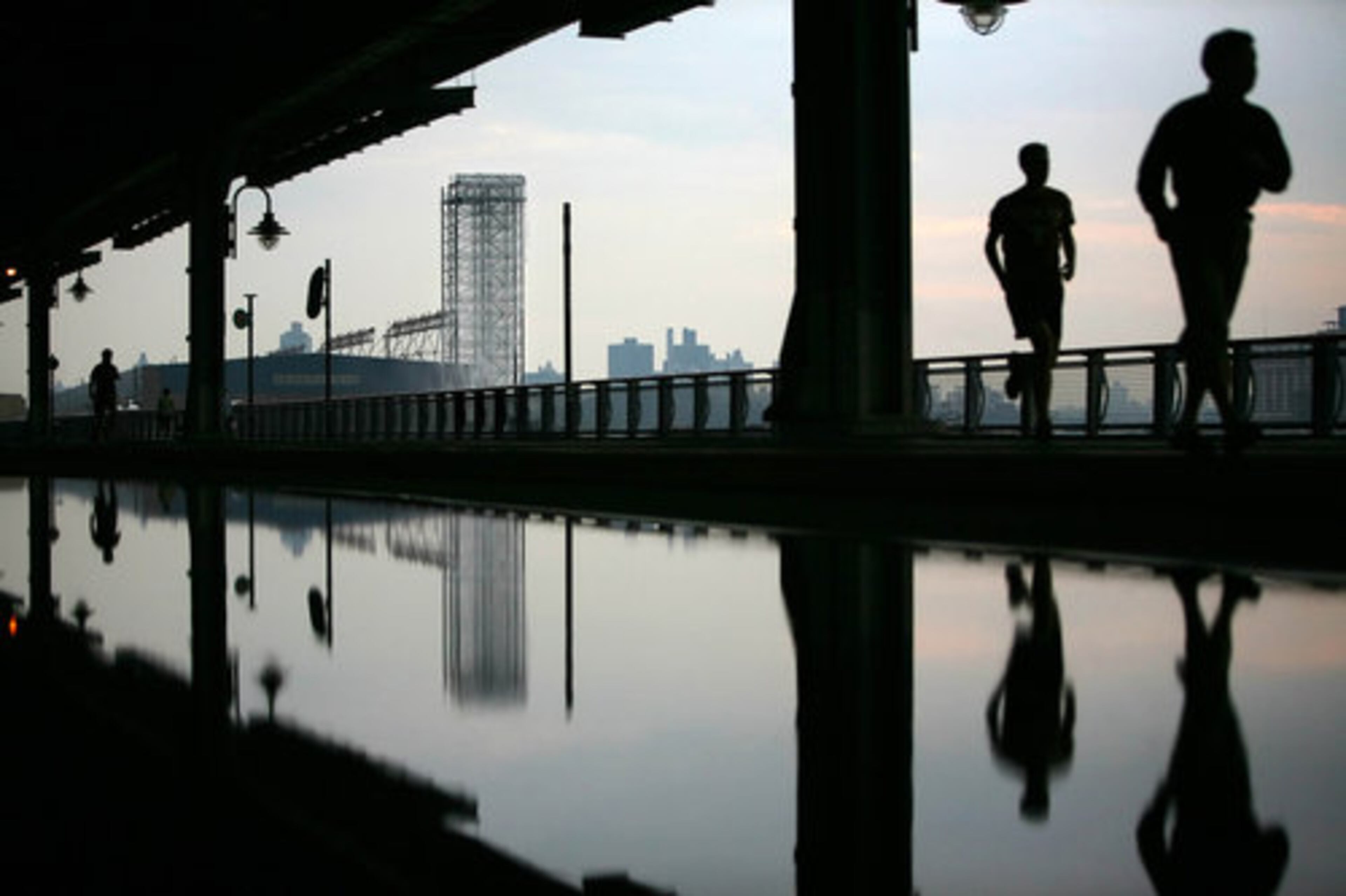 Runners are silhouetted early Thursday morning along New York's East River near Pier 35 with one of artist Olafur Eliasson's waterfall installations providing the background.