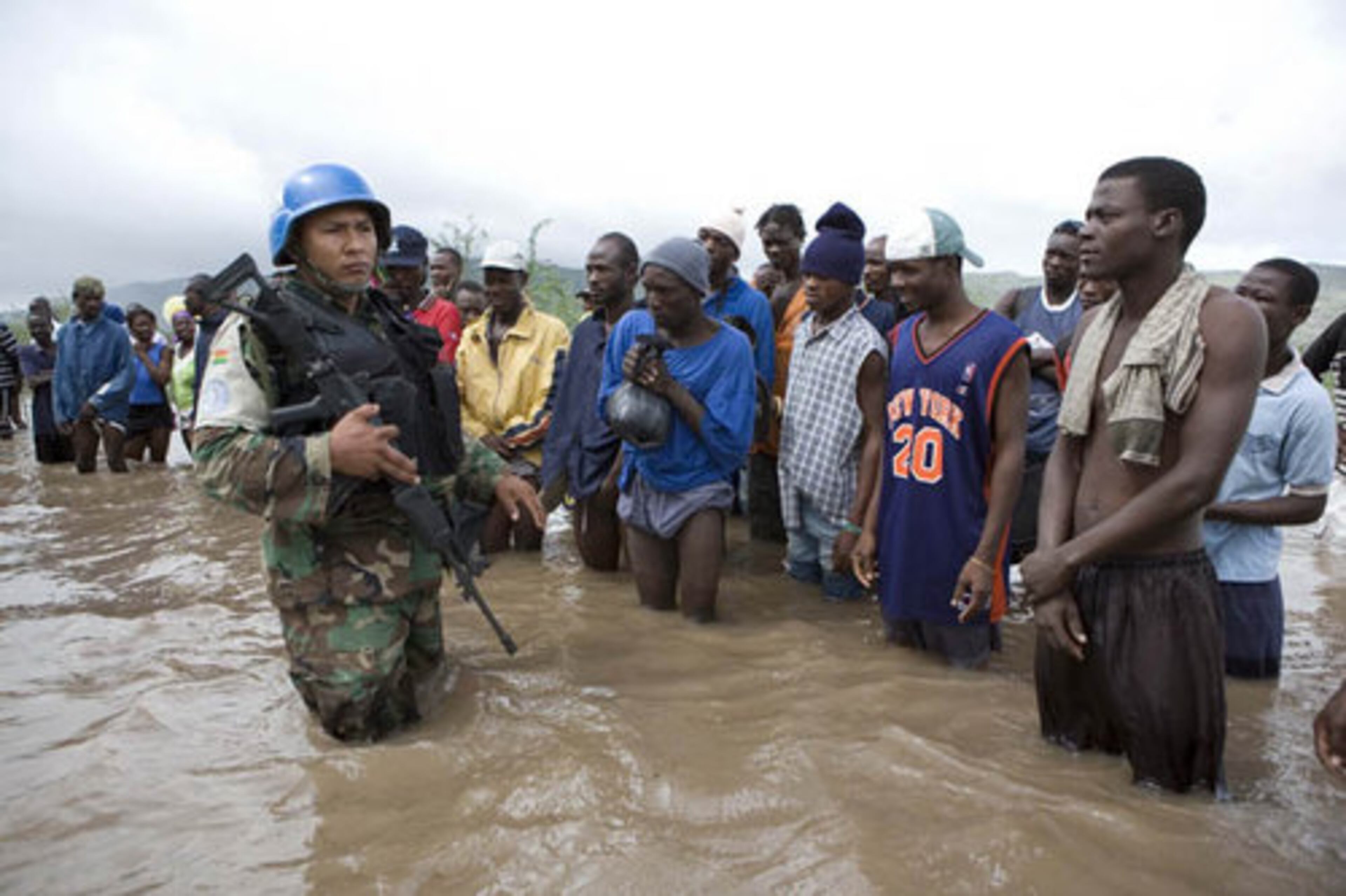 A Bolivian peacekeeper, left, stands on an area flooded by heavy rains from Tropical Storm Hanna next to residents in Savan Desole.