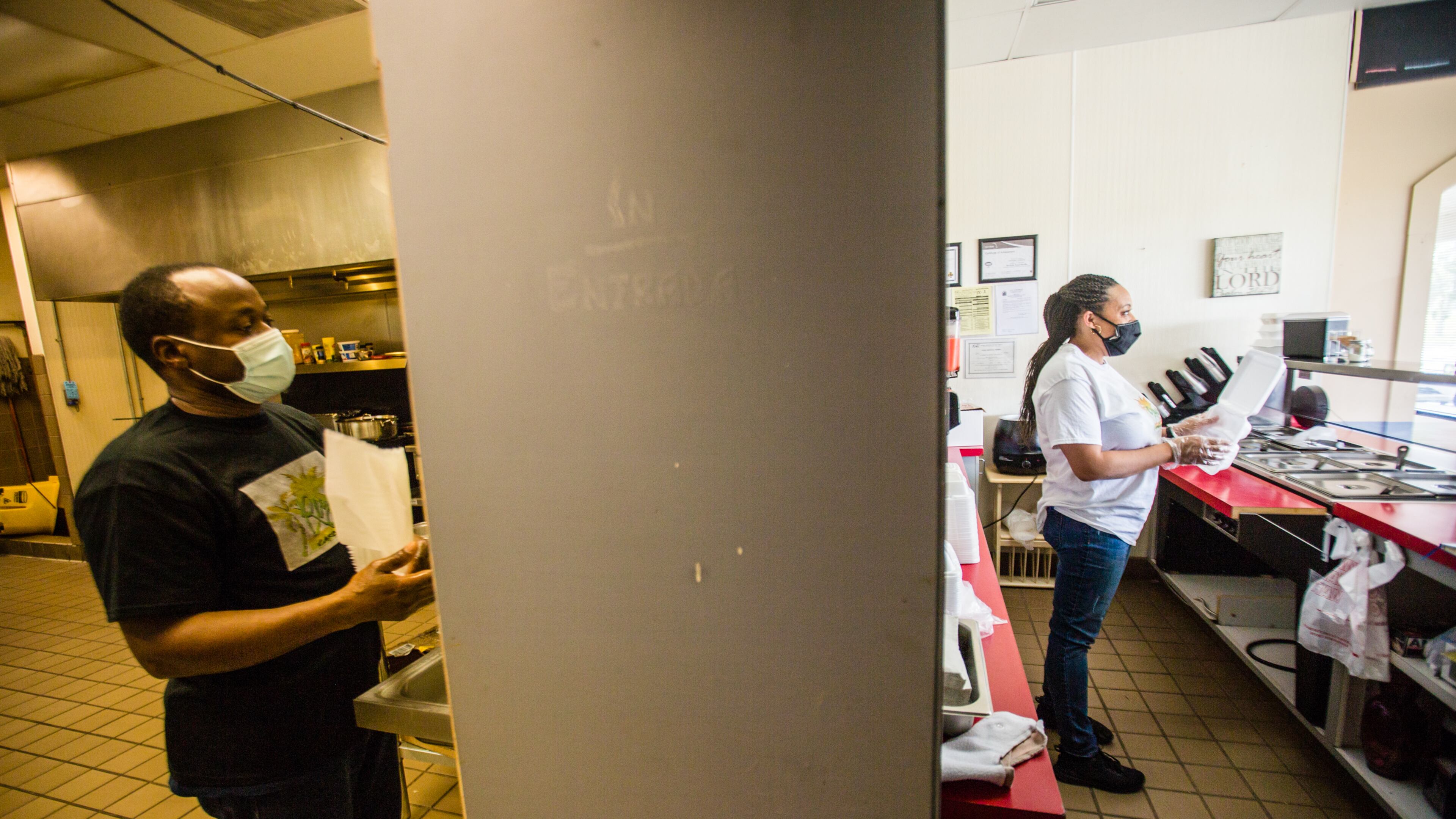 Businesses in this Hampton, GA strip mall are experiencing the effects of the pandemic differently. Floyd Johnson, left, works in the kitchen making soup and Chandra Johnson, right, fills a to-go order at Reggae Vybz on Tuesday, Sept. 8, 2020. The family-owned Caribbean restaurant is struggling to keep going without sit-in dining and delivery orders still lagging. (Jenni Girtman for The Atlanta Journal-Constitution)