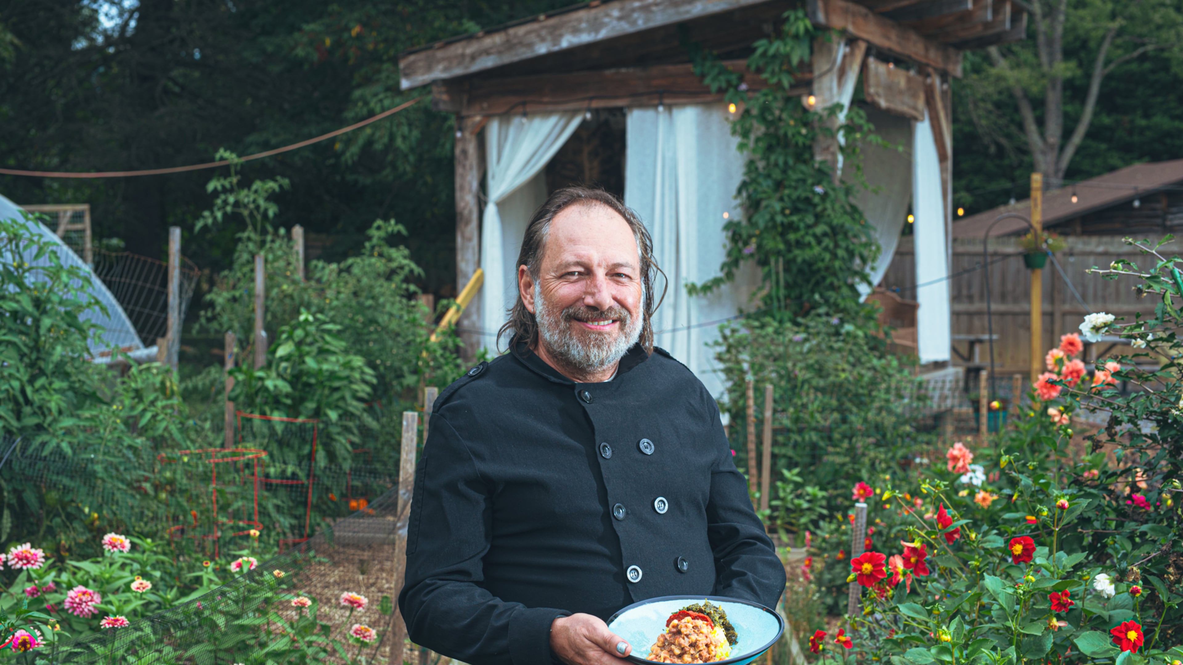 Executive chef and owner Mark Henegan of the Bush Farmhouse poses in the restaurant's garden with a bowl of his South African-inspired hoppin' John. (Grace Dickinson for The Atlanta Journal-Constitution)