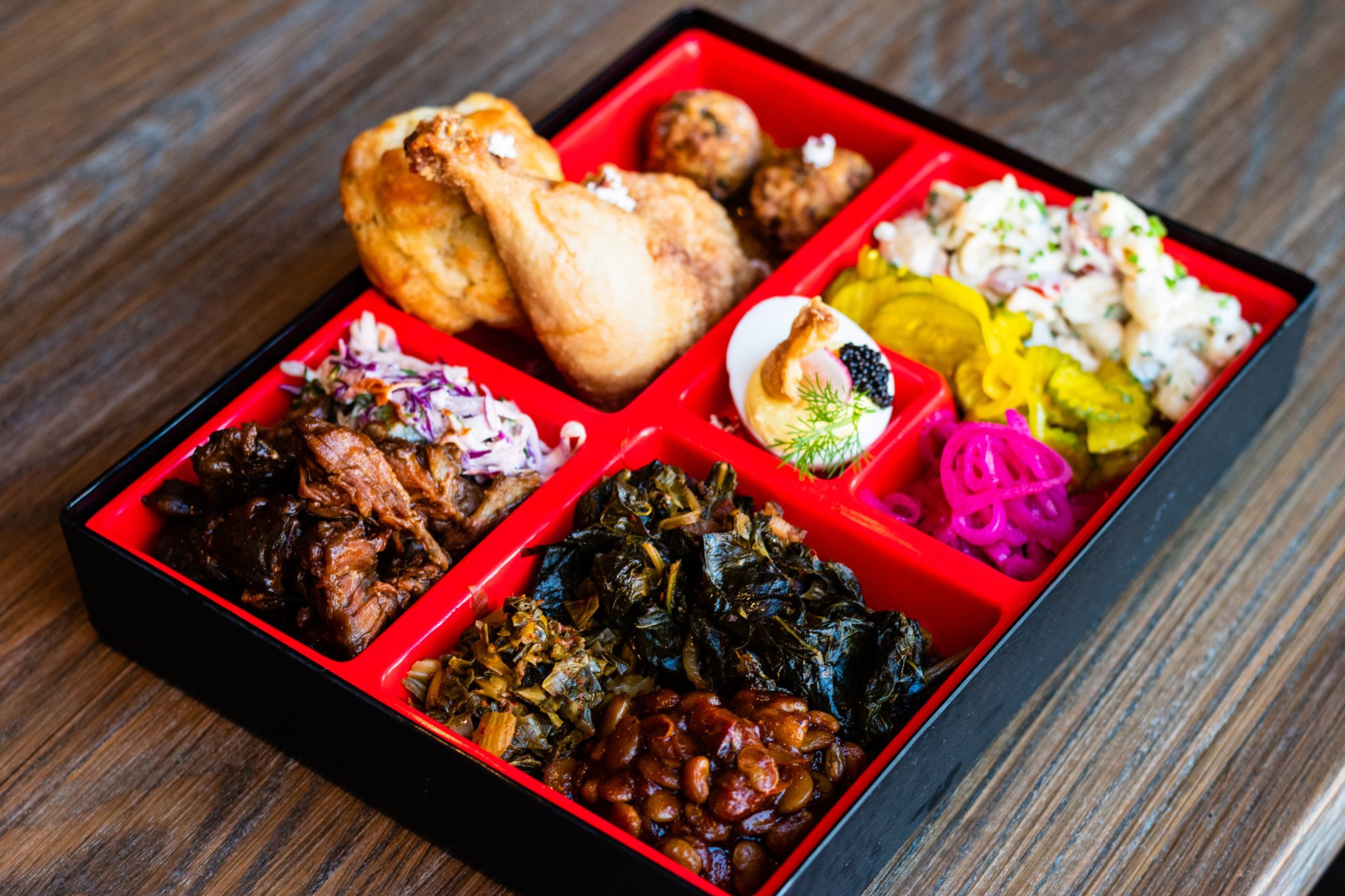 The Southern Bento Box at Watershed rotates with an offering of regional staples. Pictured are a drumstick of the restaurant’s iconic fried chicken, pulled pork, macaroni salad, deviled eggs and collard greens. CONTRIBUTED BY HENRI HOLLIS