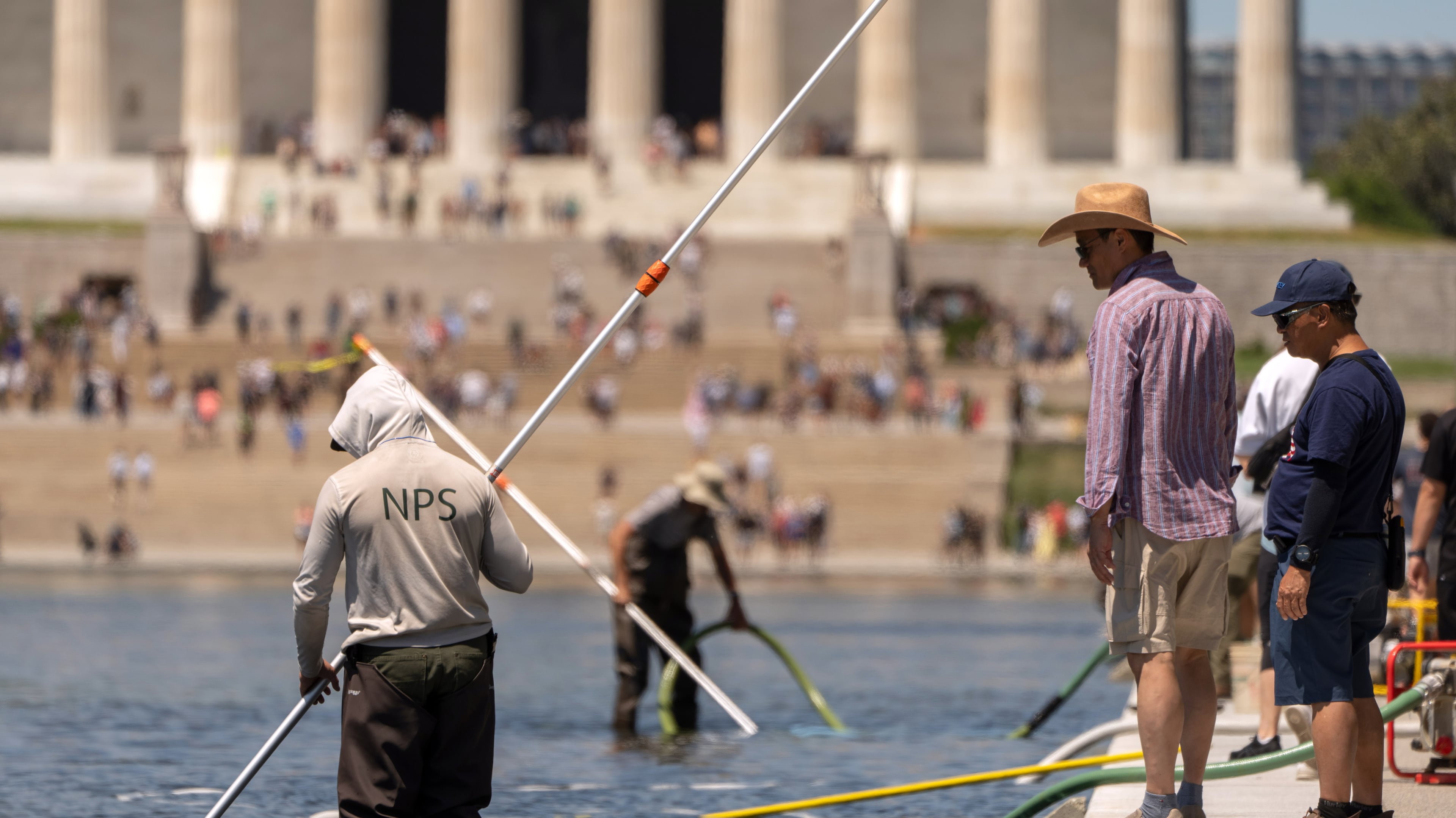 Visitors watch as National Park Service employees use vacuums to clean the Lincoln Memorial Reflecting Pool, Saturday, June 20, 2026, in Washington. (AP Photo/Mark Schiefelbein)
