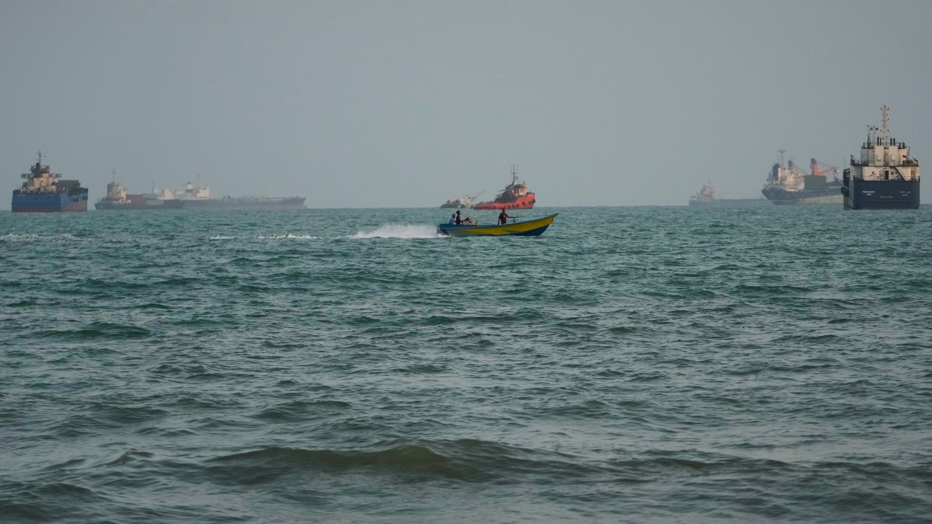 A swimmer remains near the shore as a motorboat passes commercial vessels anchored in the Strait of Hormuz off Bandar Abbas, Iran, Friday, Sept. 4, 2026. (AP Photo/Vahid Salemi)