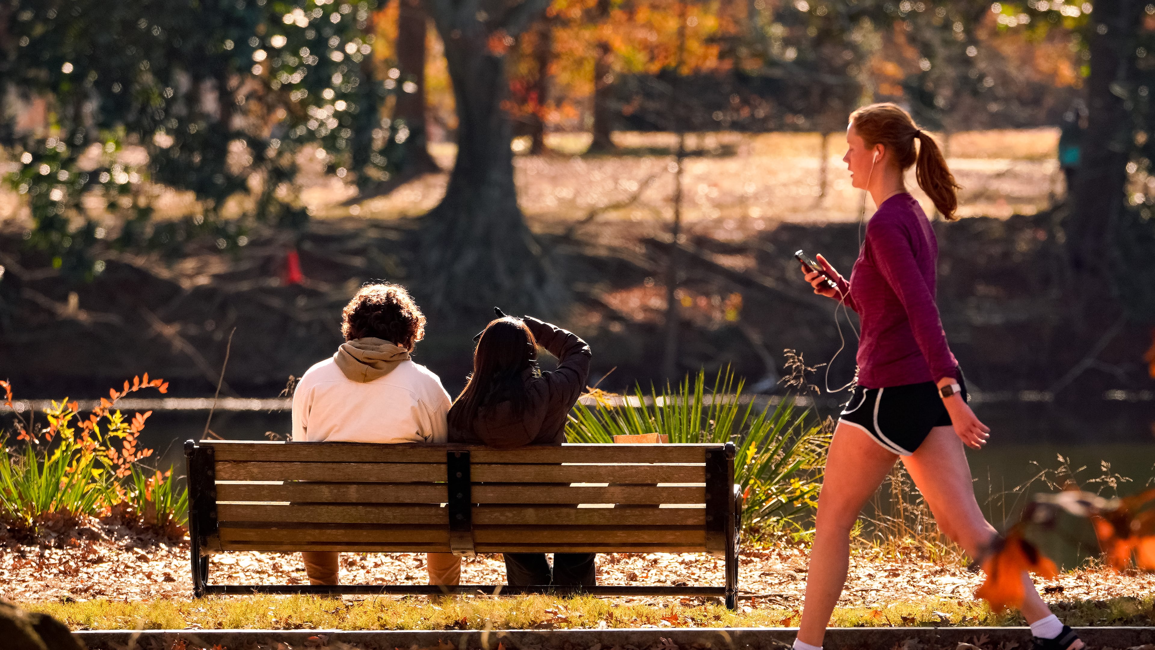 A woman walks past a couple sitting inside Piedmont Park. Tuesday, December 19th, 2023 (Ben Hendren for the Atlanta Journal Constitution)