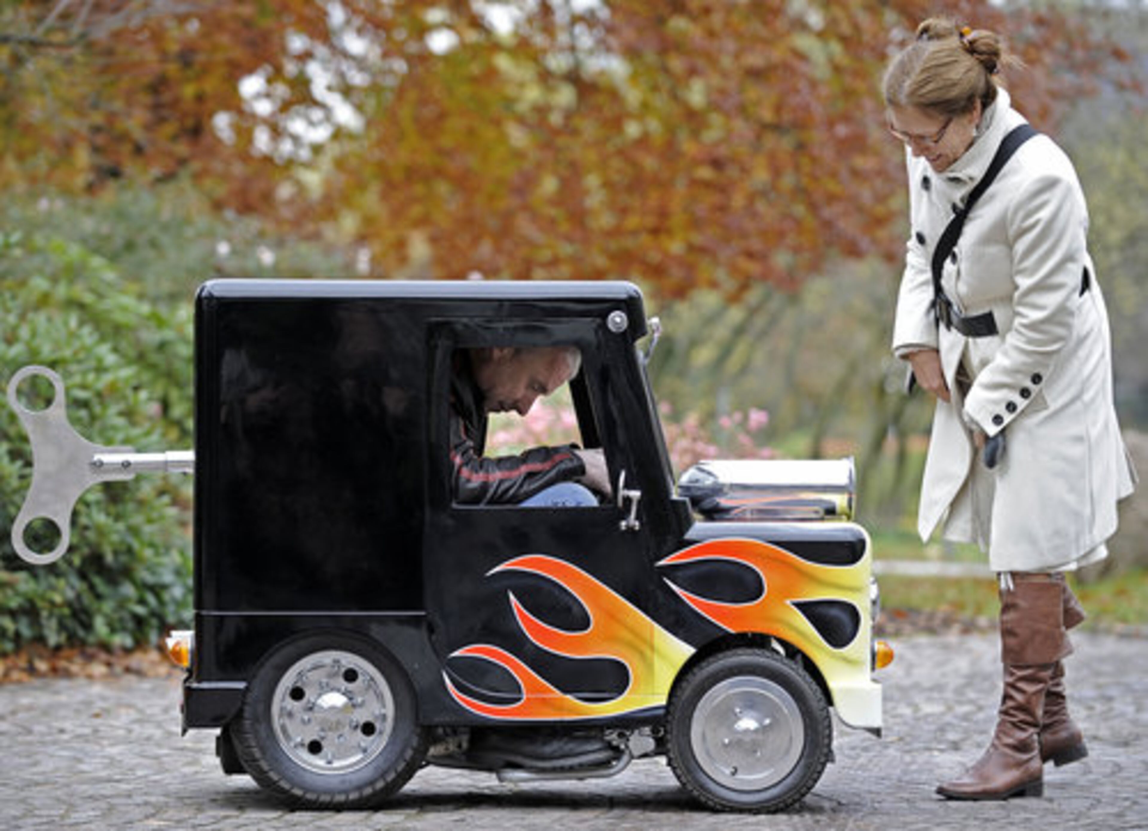 A woman watches British Perry Watkins sitting in his "Wind Up" mini car on a street in Essen, Germany, Monday, Nov. 8, 2010.