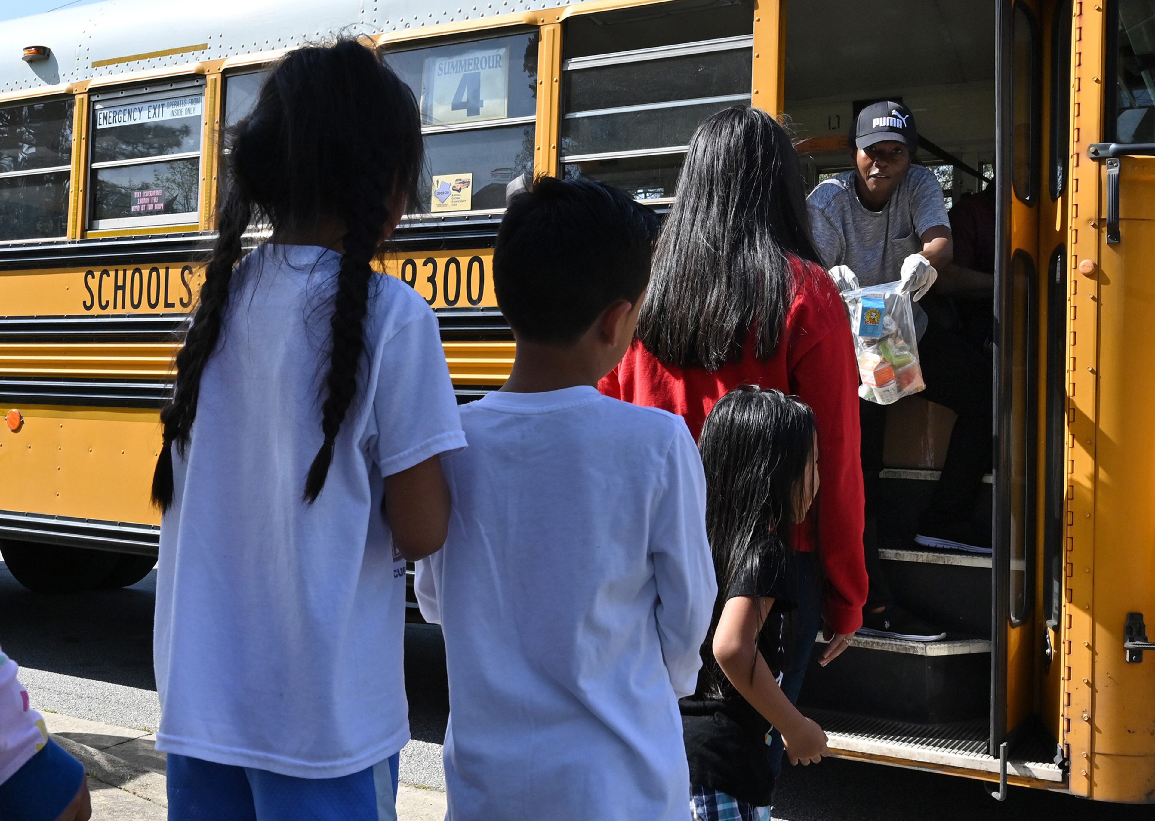 March 20, 2020 Norcross - Jocelyn Zanzala (background), school bus driver, delivers a free meal to students at their school bus stop on Friday, March 20, 2020. Gwinnett County Schools offers meal pickup at 68 sites and bus stops near the schools from 11 a.m. to 1 p.m. for children 18 and under. (Hyosub Shin / Hyosub.Shin@ajc.com)