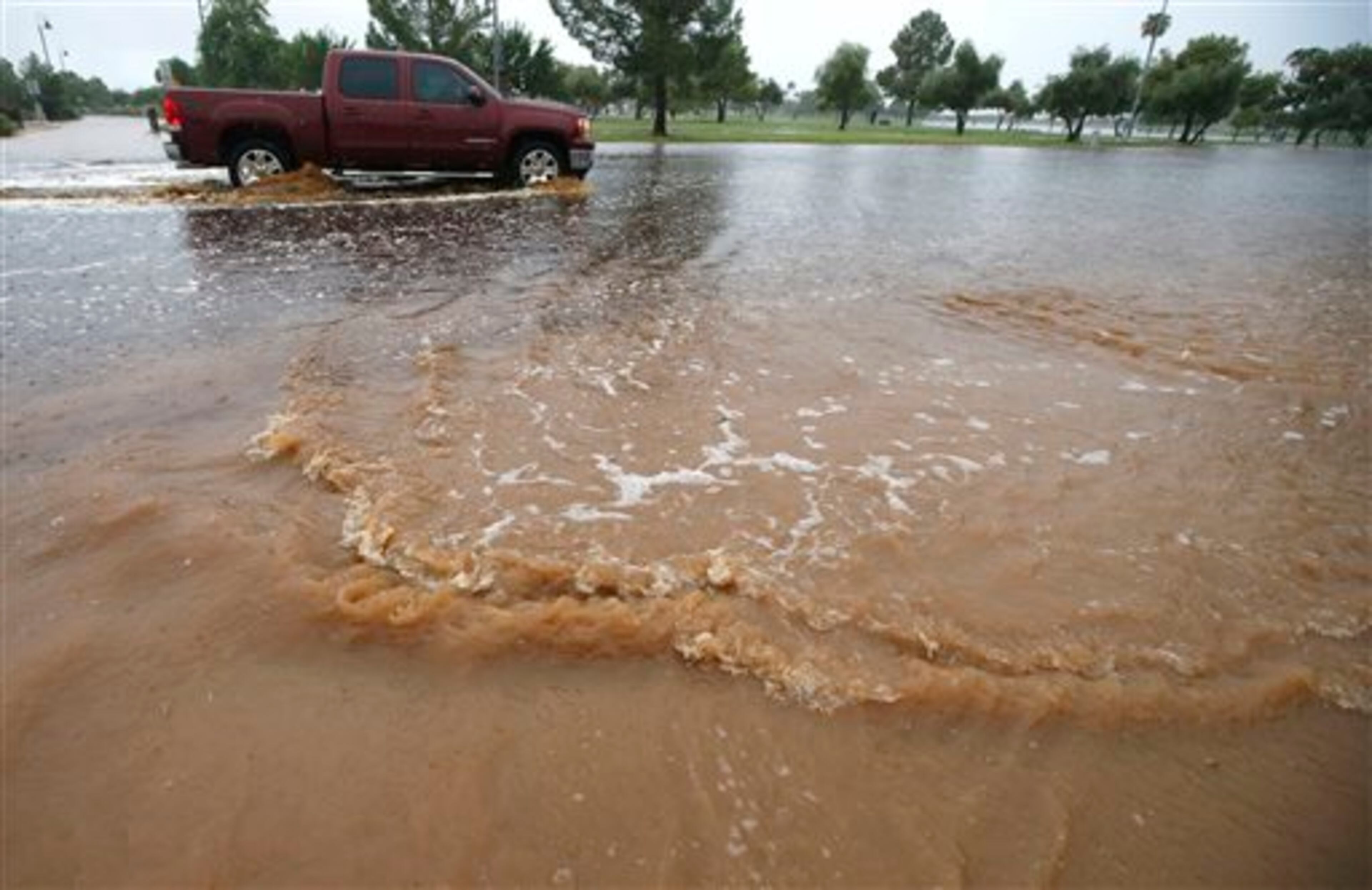 Flood waters rush into a street as a vehicle moves into deeper flash flood waters as heavy rains pour down Monday, Sept. 8, 2014, in Phoenix. Storms that flooded several Phoenix-area freeways and numerous local streets during the Monday morning commute set an all-time record for rainfall in Phoenix in a single day. (AP Photo/Ross D. Franklin)