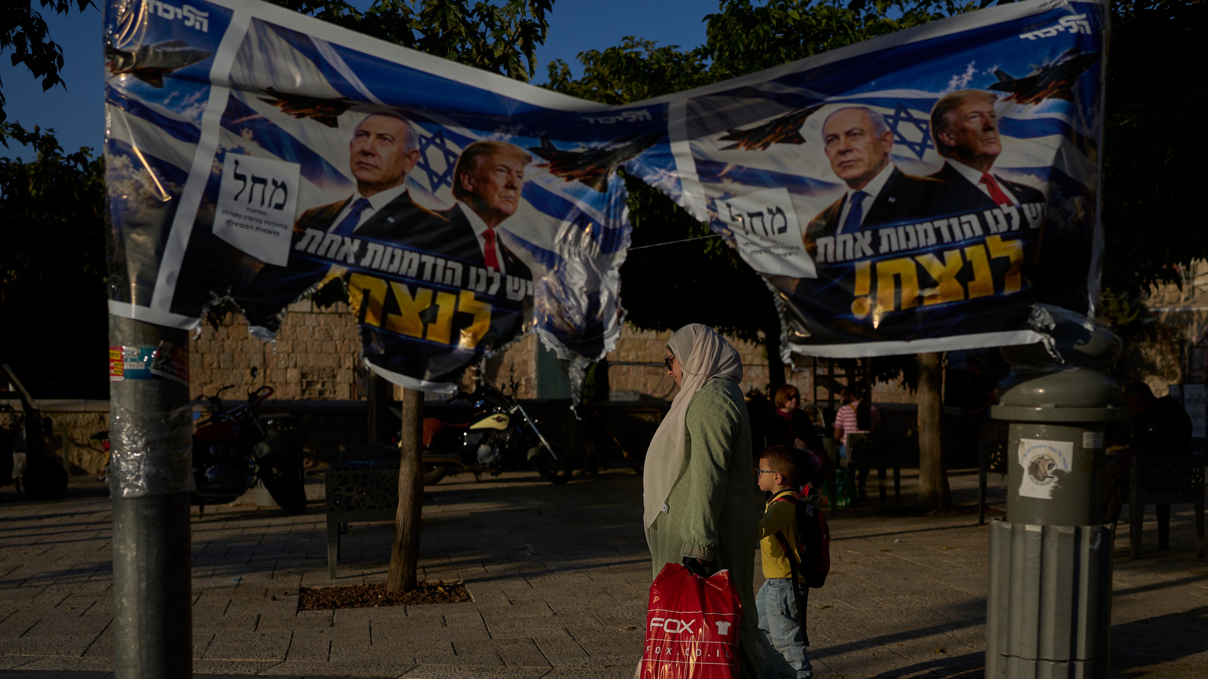 An Arab woman walks with a child next to a torn Likud party campaign ad featuring Israeli Prime Minister Benjamin Netanyahu and U.S. President Donald Trump, with a Hebrew message reading "We have one opportunity to win," in Jerusalem on Wednesday, Oct. 28, 2026, a day after the elections in Israel. (AP Photo/Ohad Zwigenberg)