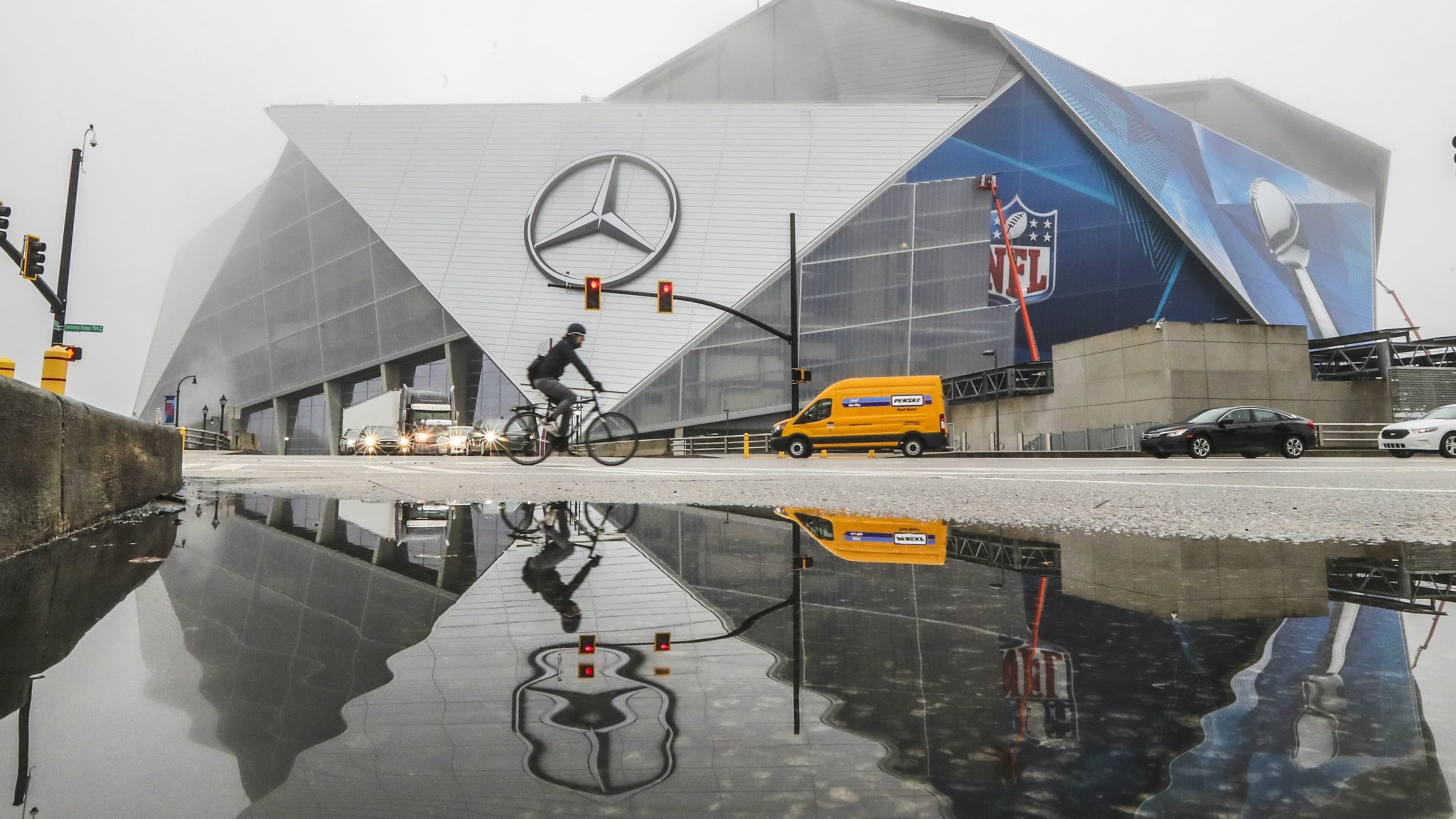 Work continued on Mercedes-Benz Stadium adhering Super Bowl graphics across the facade reflected in puddled water along Martin Luther King Jr. Drive in downtown Atlanta. A group of residents claims the stadium should be paying property taxes. JOHN SPINK/JSPINK@AJC.COM