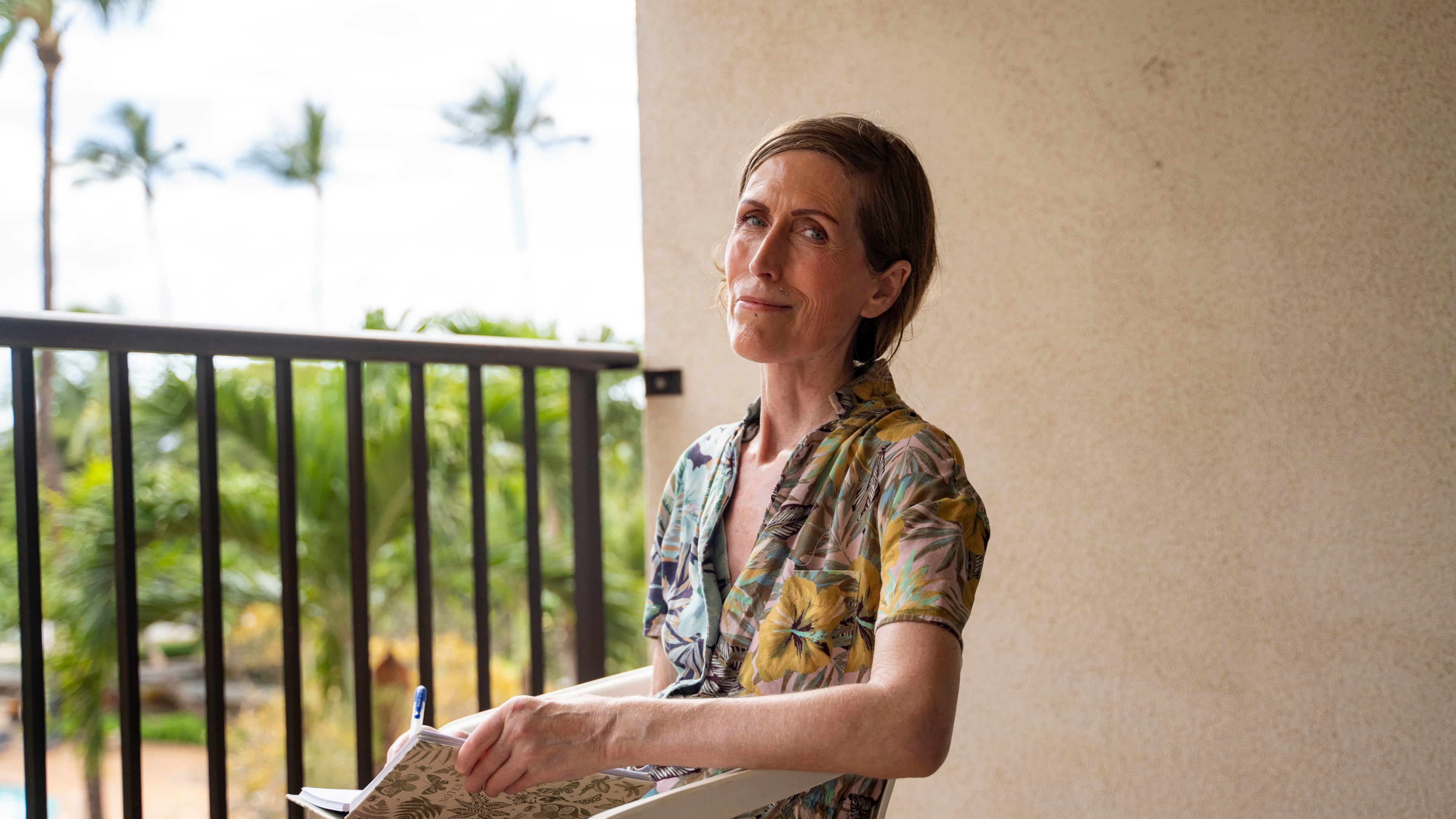 Mari Younger poses for a portrait on the balcony of her converted hotel room where she lives after being displaced by the Maui fires two years prior, in Kihei, Hawaii, Wednesday, March 4, 2026. (AP Photo/Mengshin Lin)