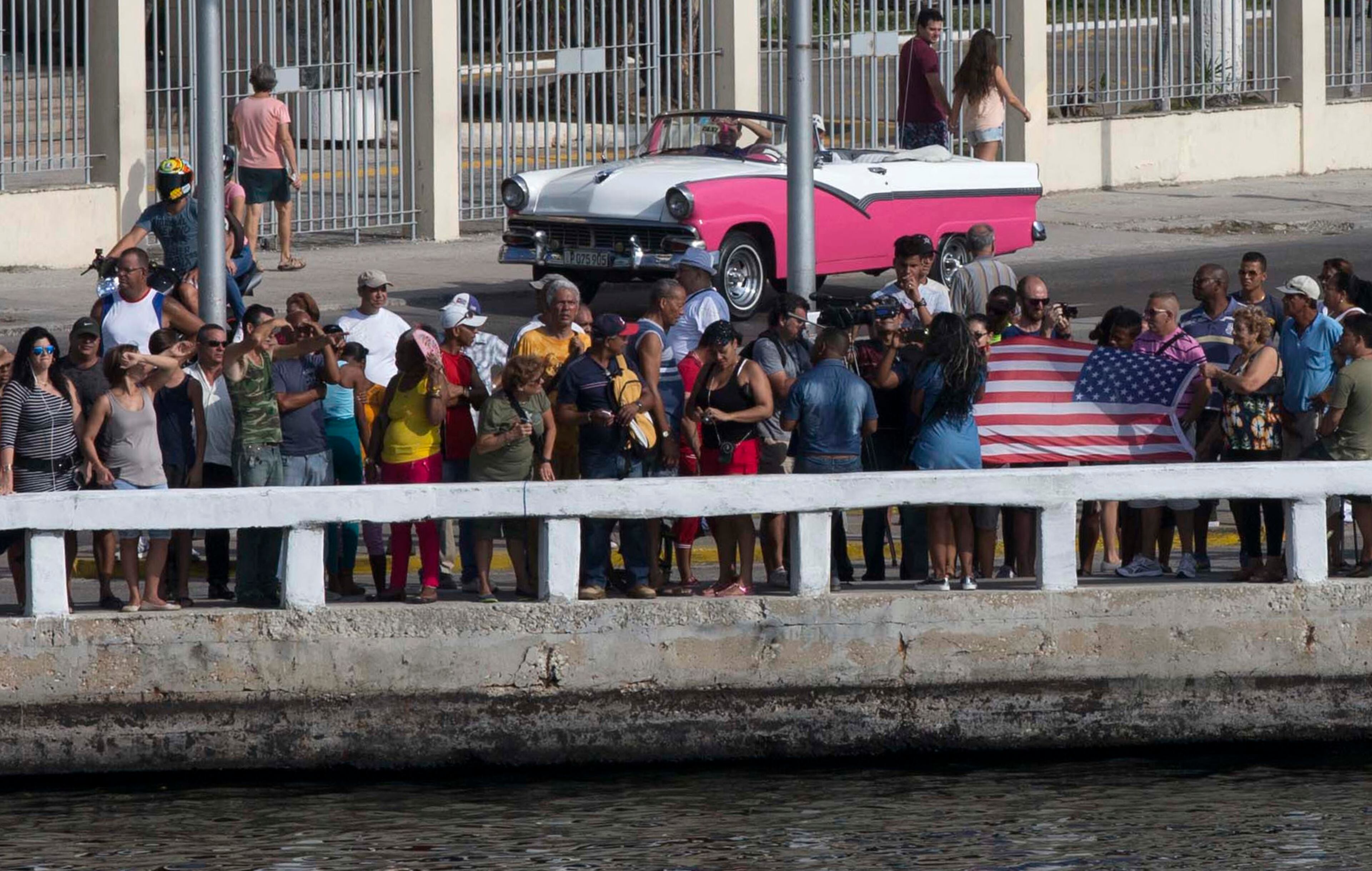 People display a U.S. flag as they wait for Carnival's Adonia cruise ship to arrive from Miami, in Havana, Cuba, Monday, May 2, 2016. The Adonia's arrival is the first step toward a future in which thousands of ships a year could cross the Florida Straits, long closed to most U.S.-Cuba traffic due to tensions that once brought the world to the brink of nuclear war. (Ismael Francisco/Cubadebate via AP)