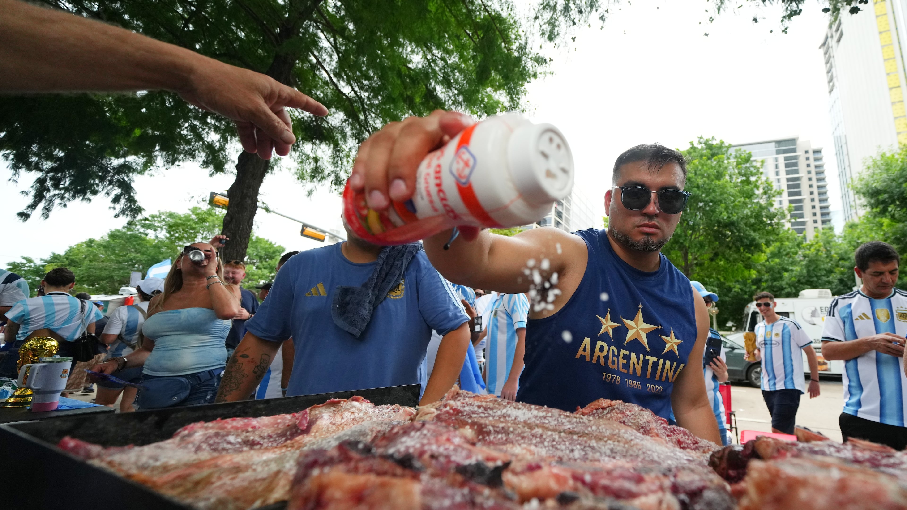Lucas Martinez, of Dallas, an Argentina supporter, seasons meat with salt while grilling during a rally ahead of their team's World Cup Group J soccer match against Austria, Sunday, June 21, 2026, in Dallas. (AP Photo/Julio Cortez)